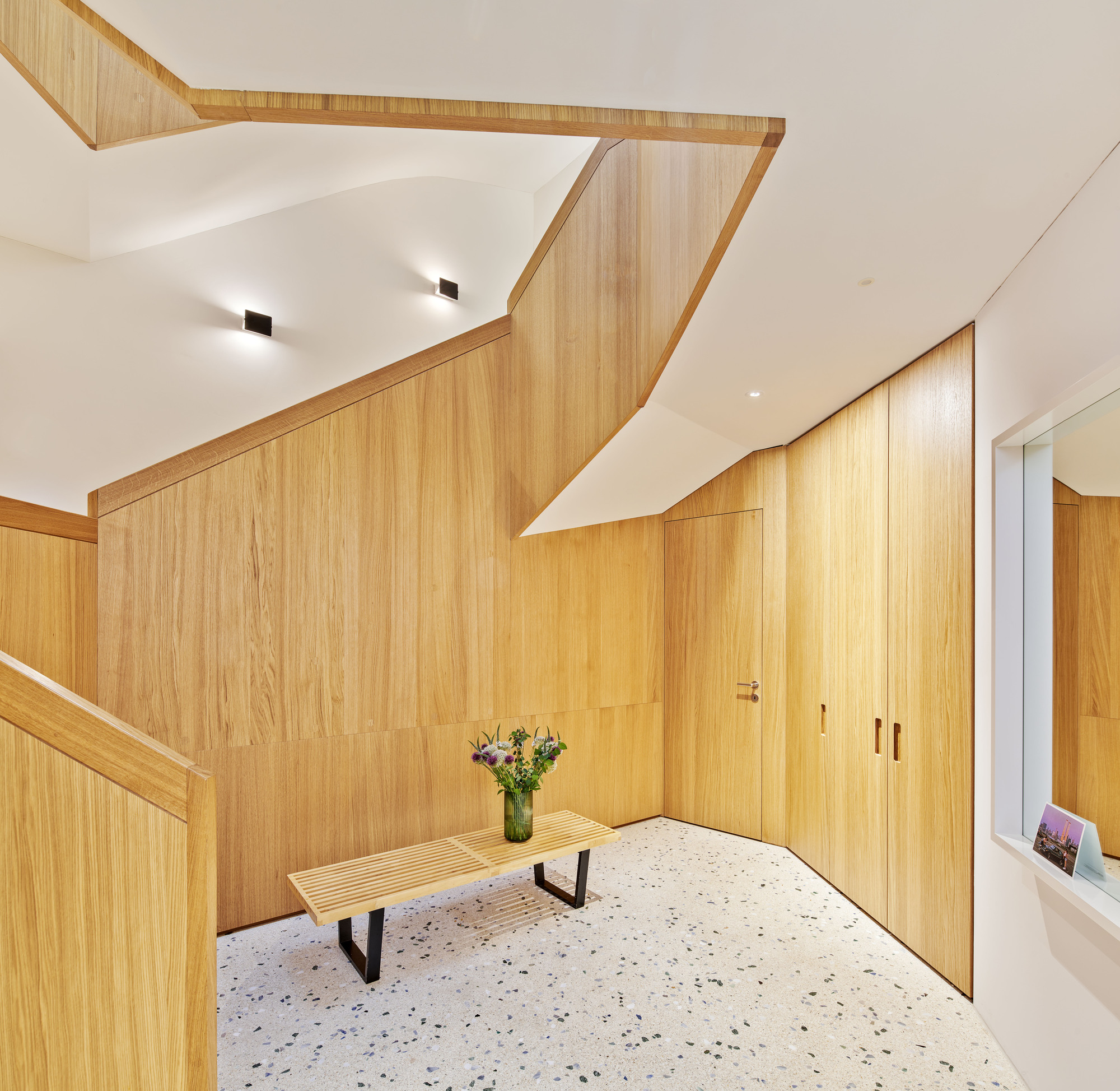 Entry hall with faceted timber-clad wall and ceiling volumes wrapping the staircase