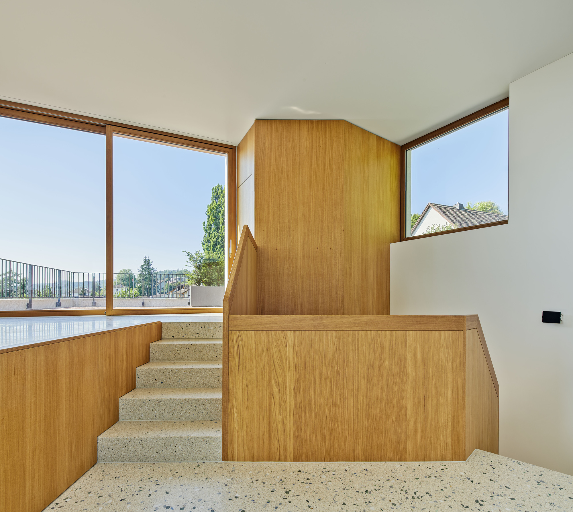 Terrazzo staircase with timber balustrade wrapping around a corner window overlooking distant rooftops