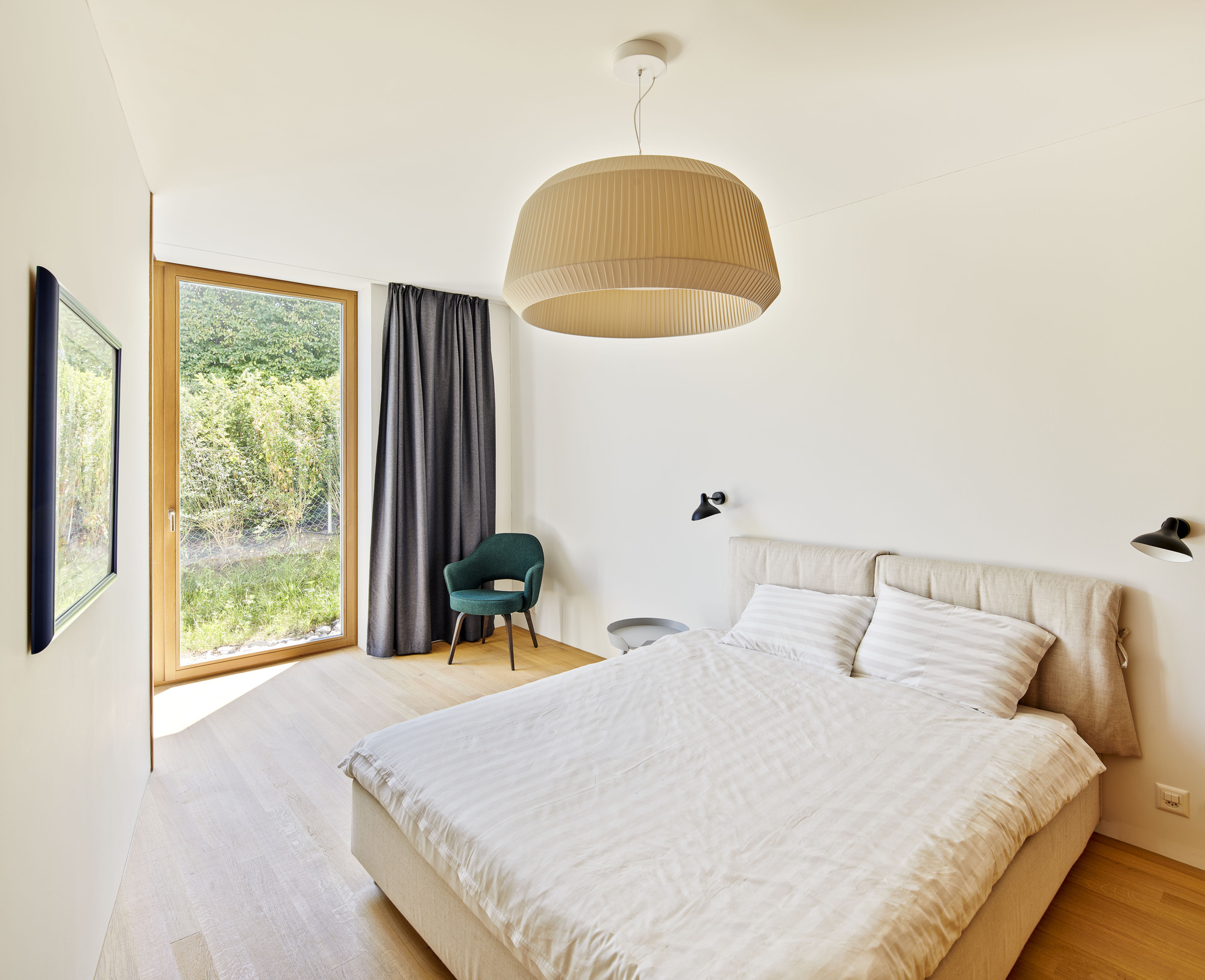 Bedroom with timber-framed window opening to a garden view and pendant light fixture overhead