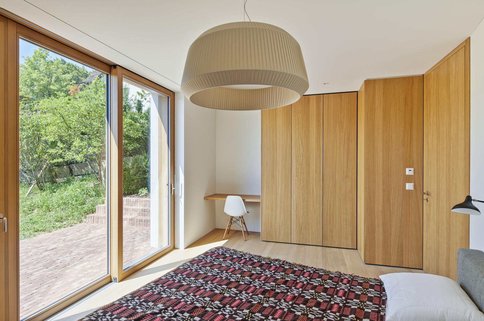 Bedroom with sliding glass door opening to a brick terrace and timber storage wall
