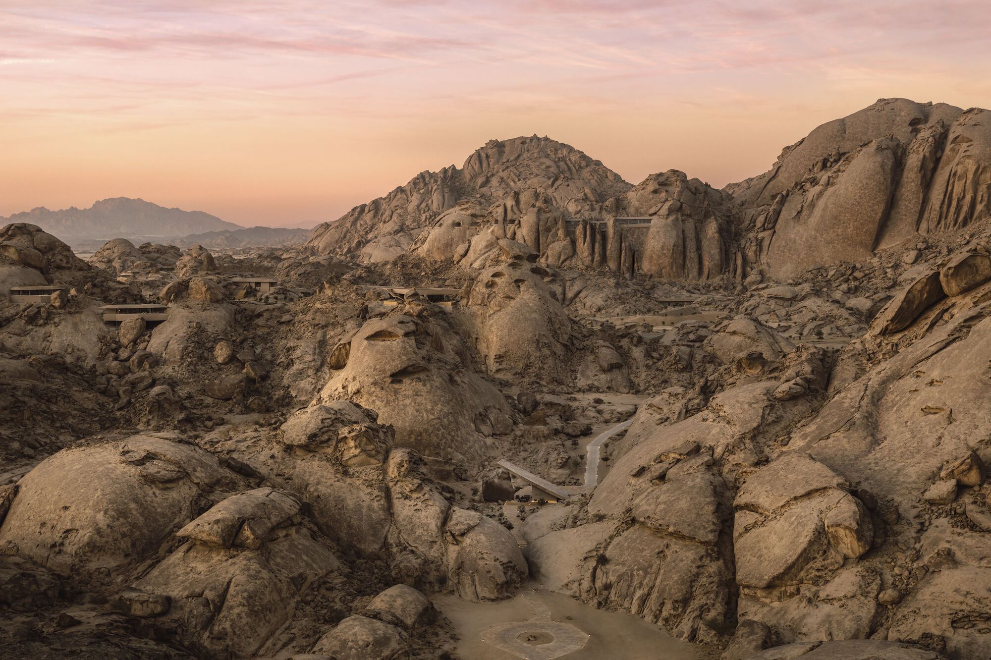Distant view of structures carved into rocky hillside at dusk with winding pathways below