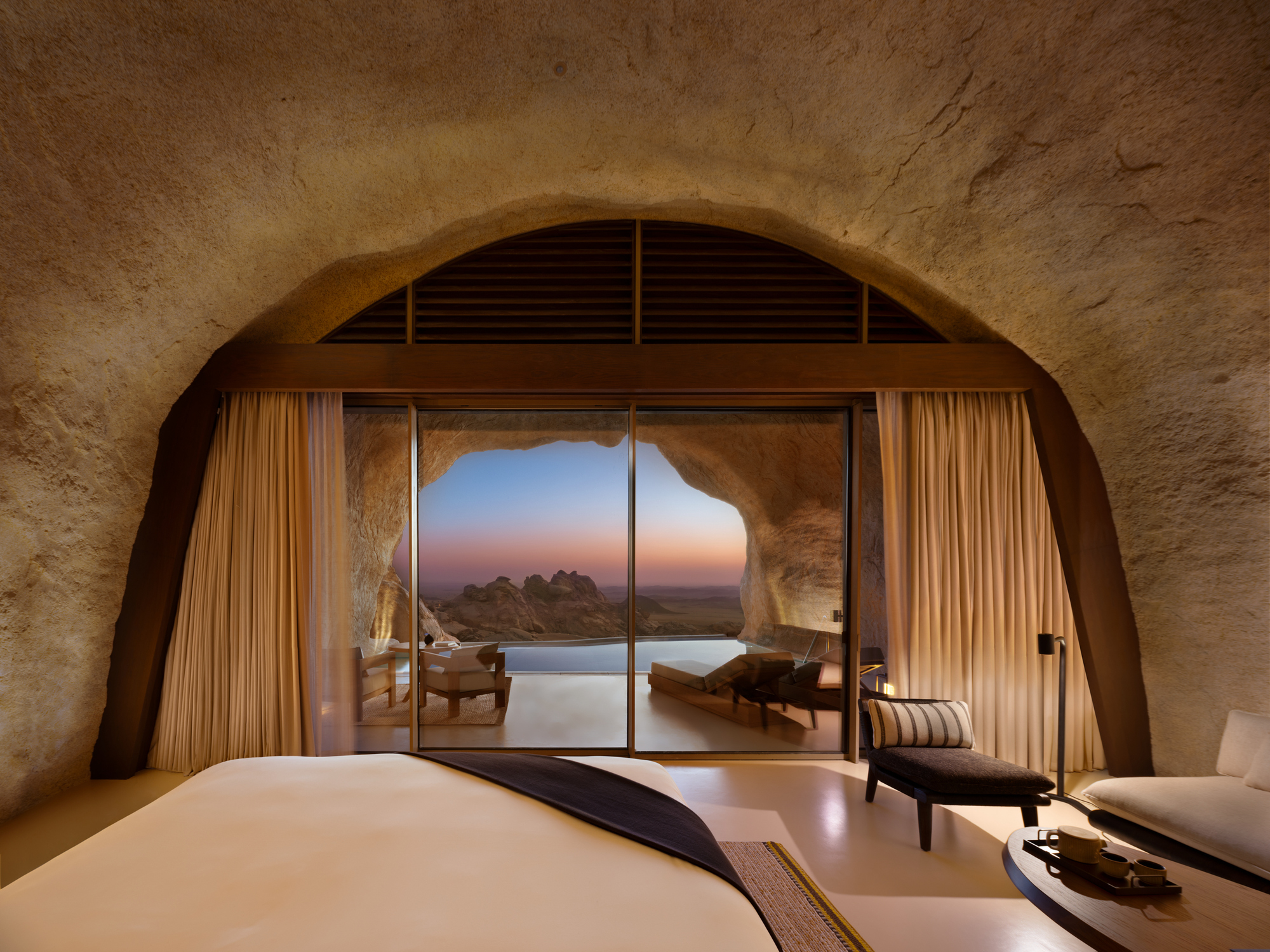 Bedroom with arched sandstone ceiling and glazed opening to pool terrace at dawn