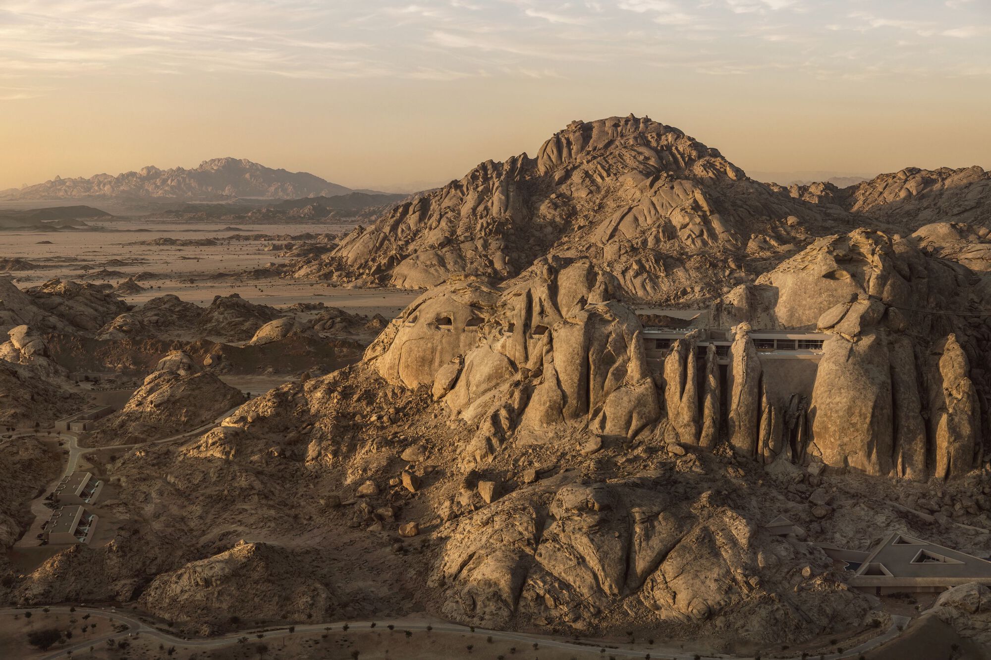 Rock-carved facade with vertical openings integrated into the desert hillside under warm afternoon light