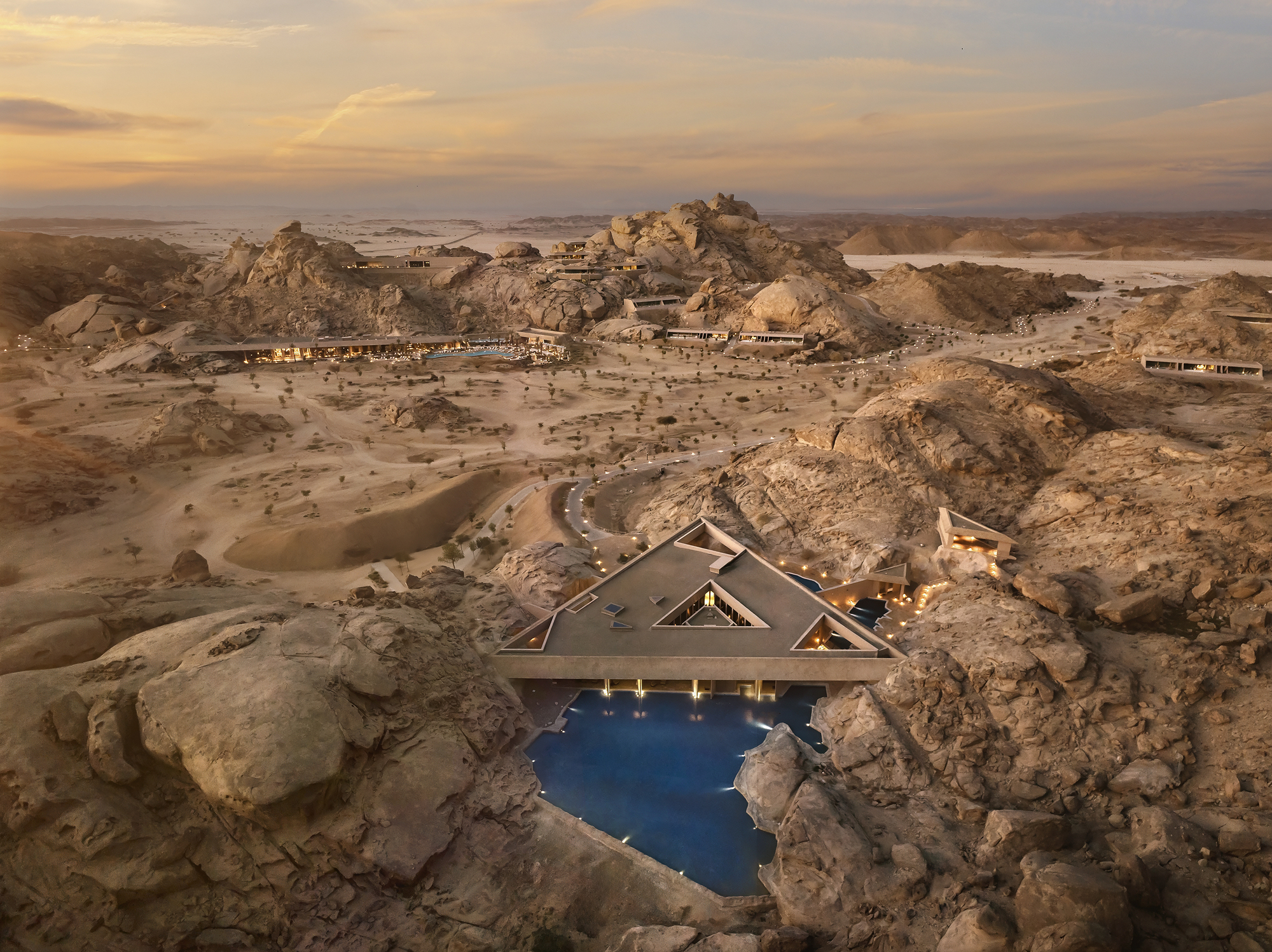 Triangular pool pavilion with cantilevered roof set among boulder formations in the desert at sunset