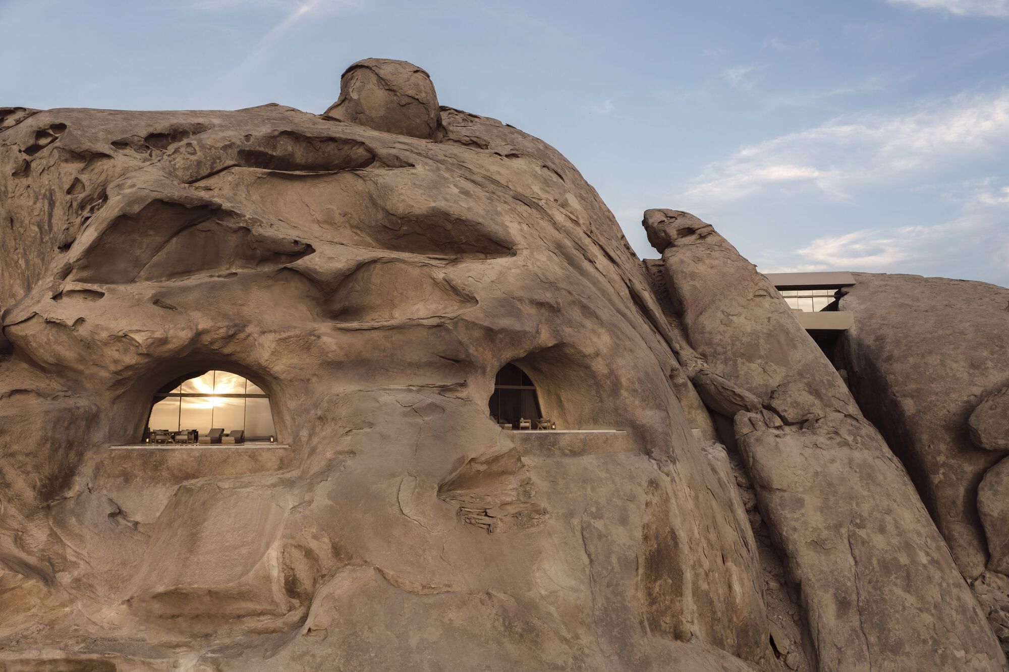 Carved window openings cut into the weathered sandstone boulder under afternoon clouds