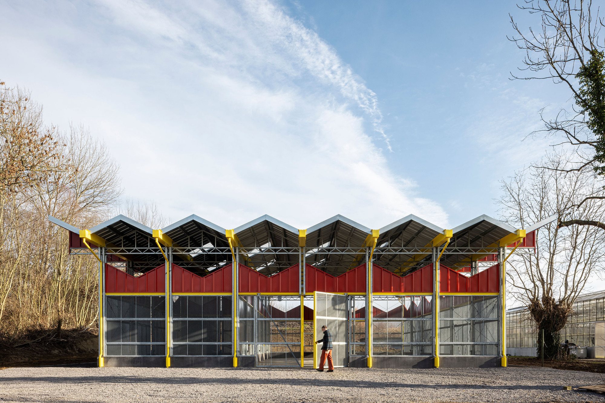 Facade with repeating sawtooth roof bays supported by yellow steel columns with red panels and glazing below