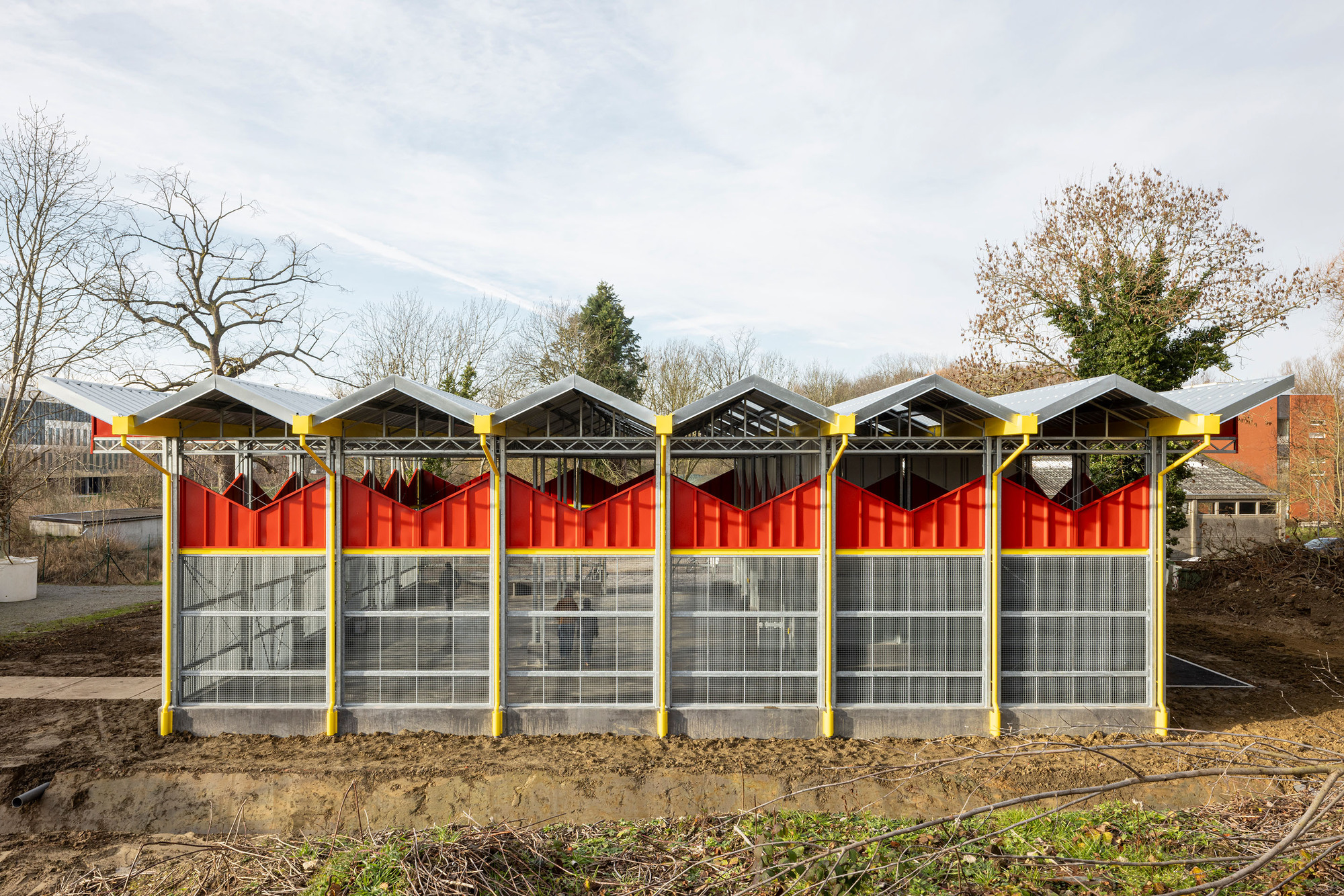 Front elevation showing six bays with red corrugated panels and glazed lower sections under a cloudy sky