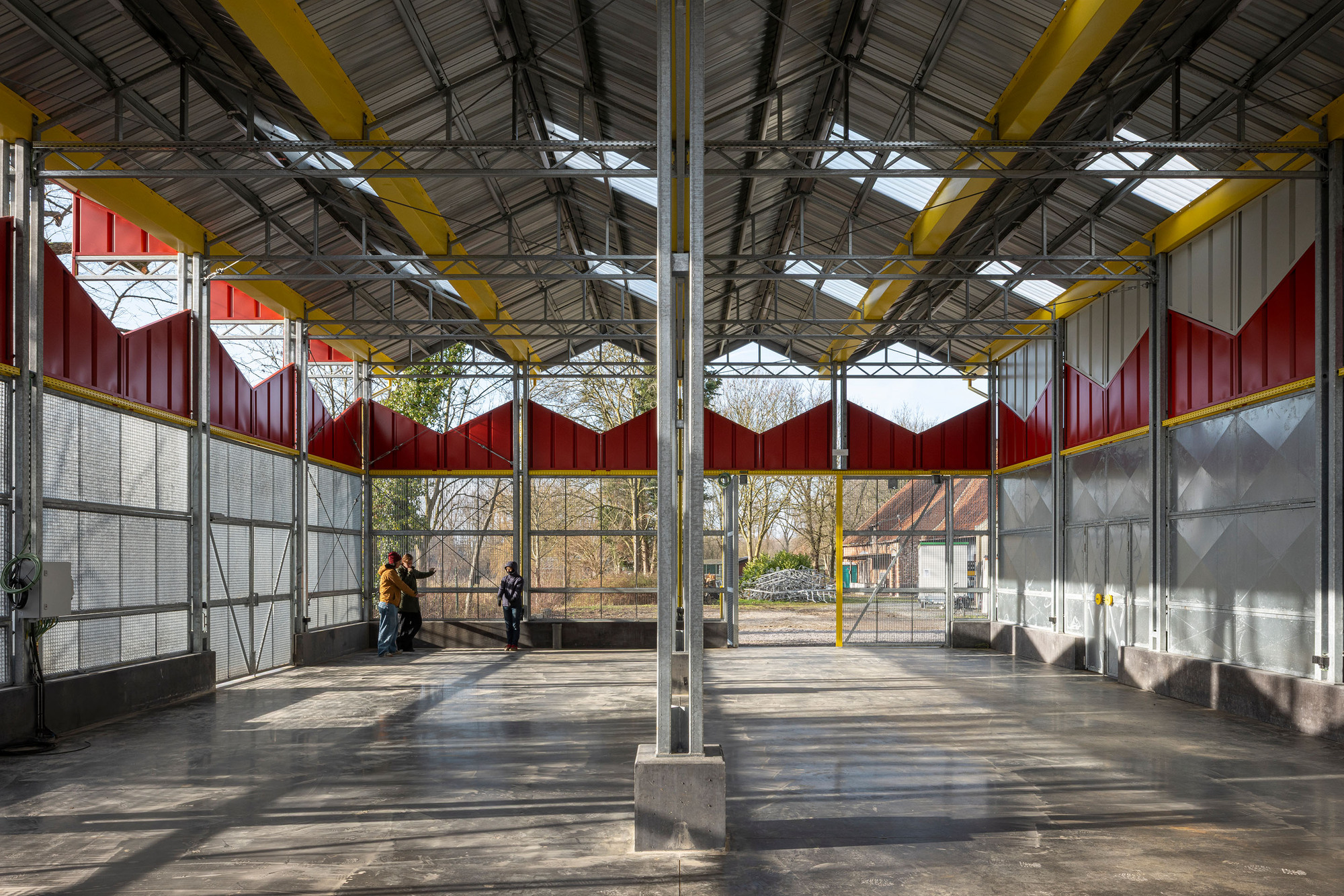 Interior space with exposed steel trusses and yellow columns beneath the corrugated metal roof with skylights
