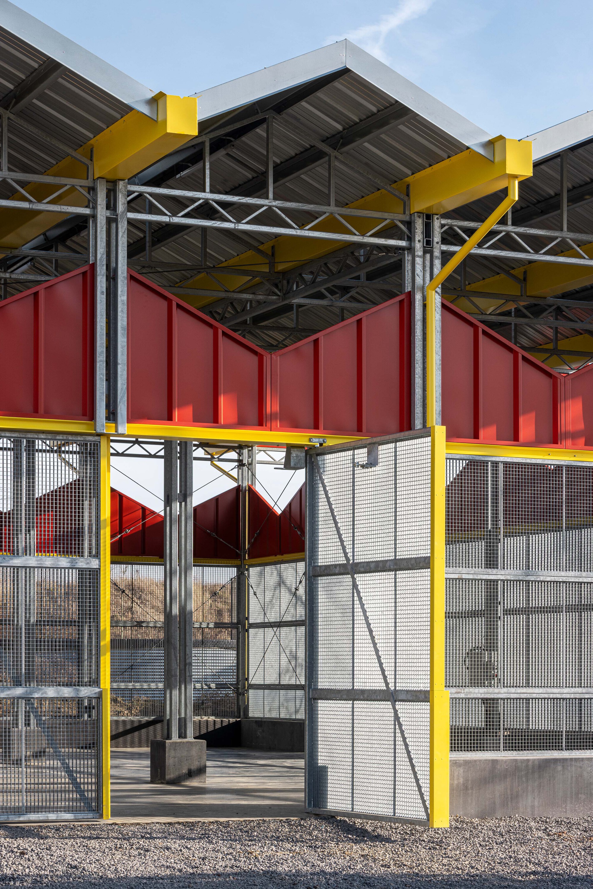 Detail of the structural frame showing yellow steel beams supporting red panels and metal mesh screening