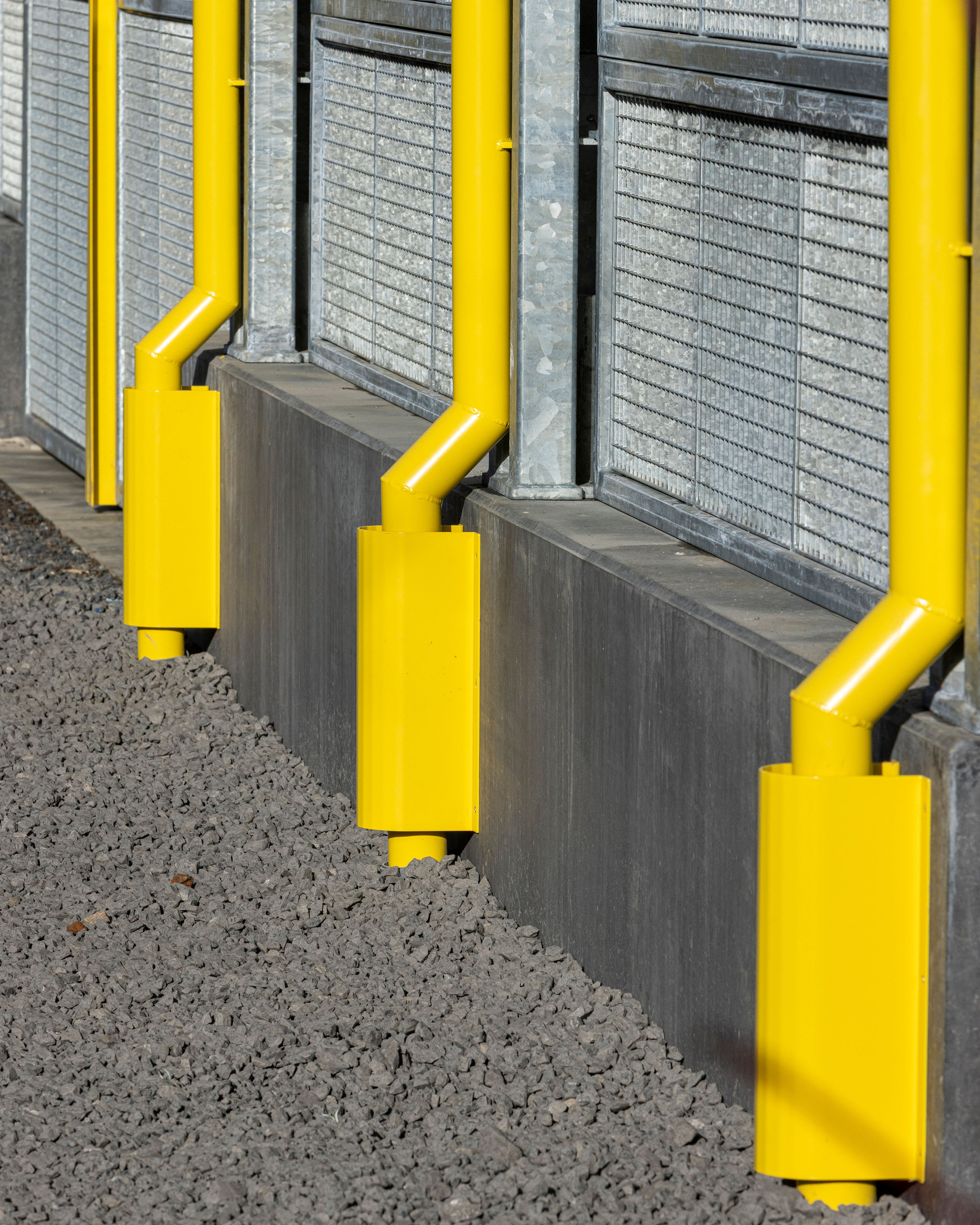 Yellow steel column bases meeting concrete foundation walls on gravel alongside wire mesh screens