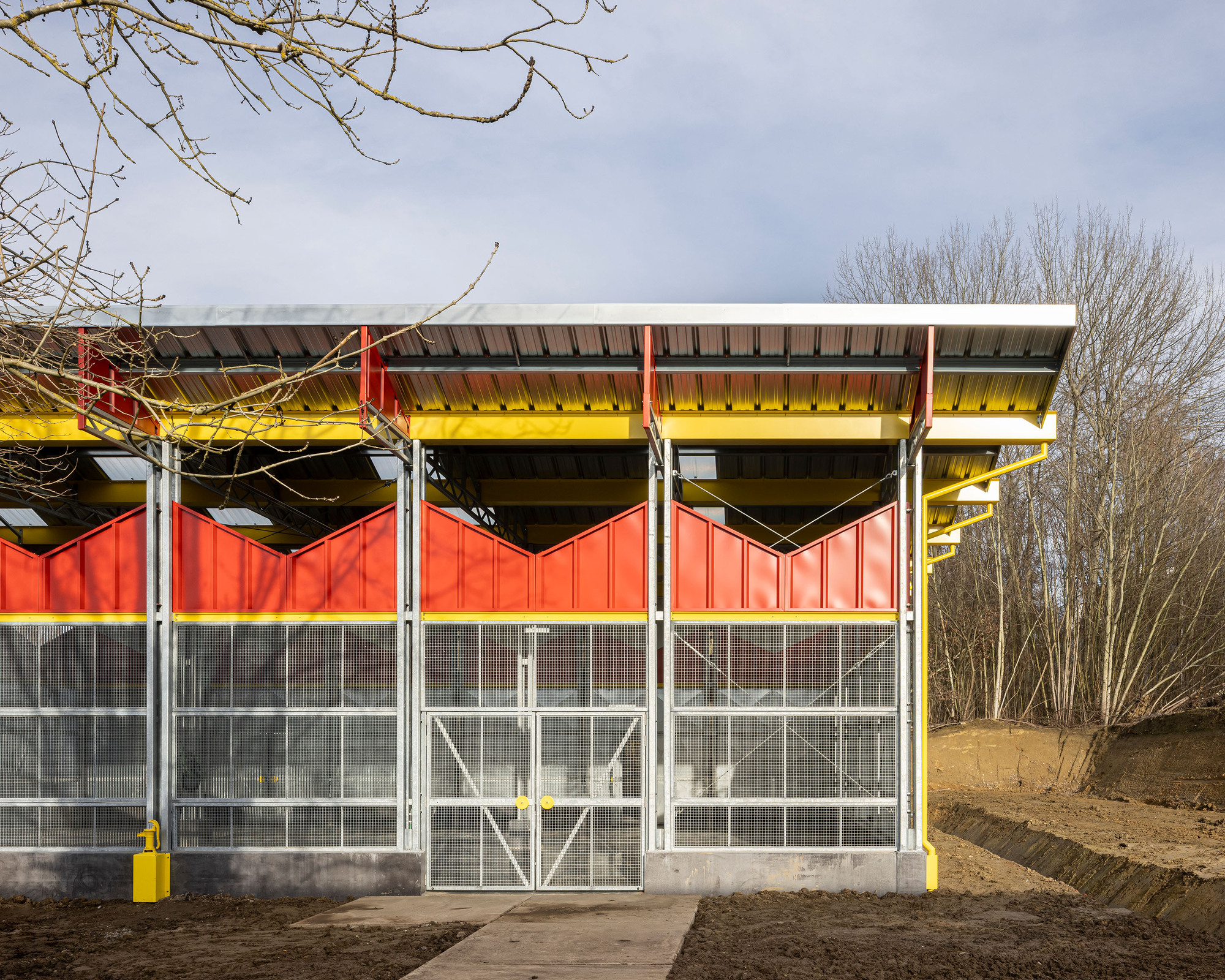 Elevation showing the galvanized mesh walls and red upper panels under bare winter trees