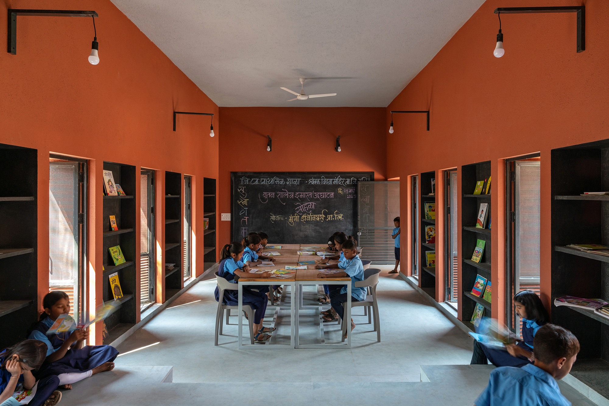 Classroom with terracotta walls and students seated at central tables under pendant light fixtures