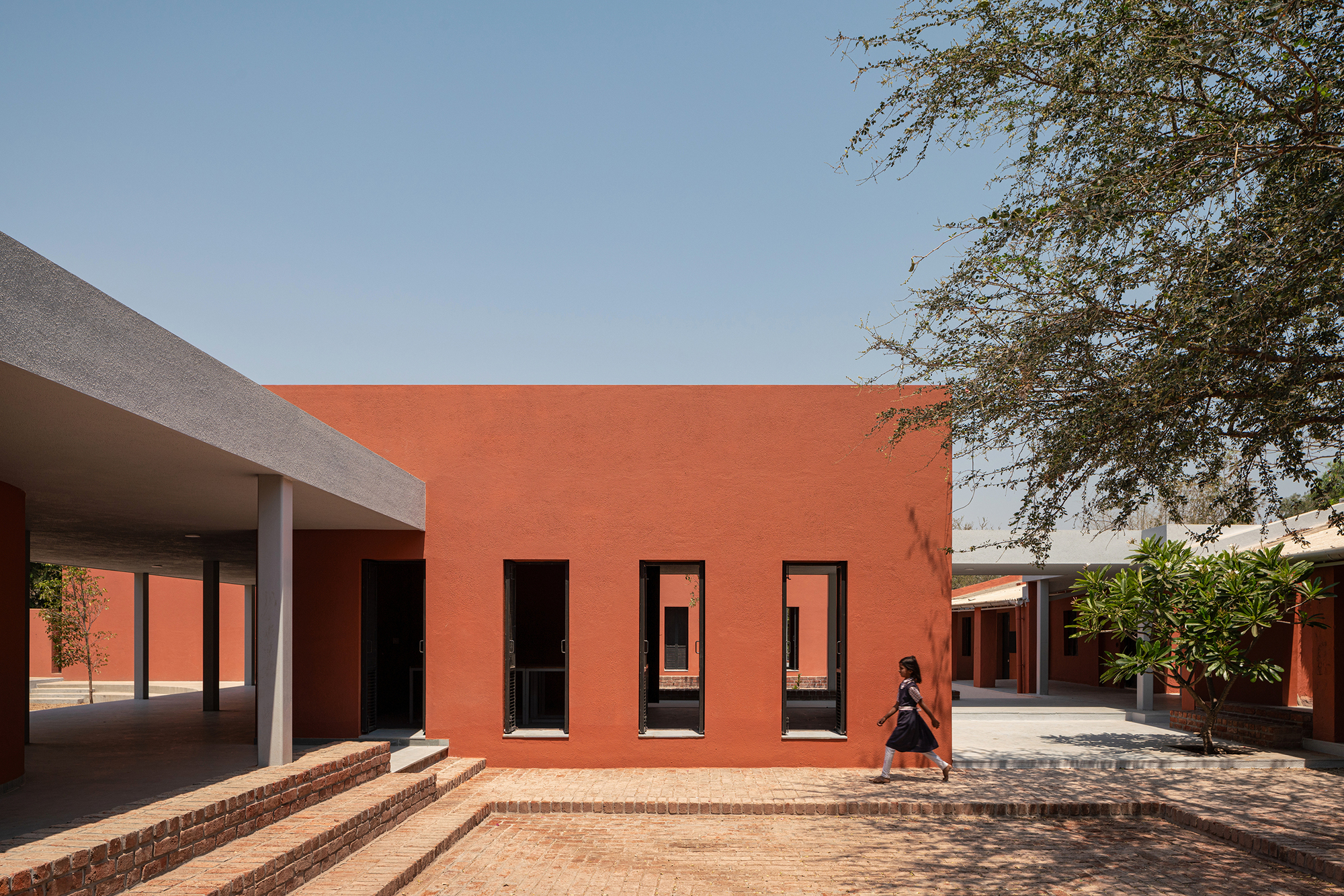 Orange facade with three tall openings overlooking a brick-paved courtyard under midday sun