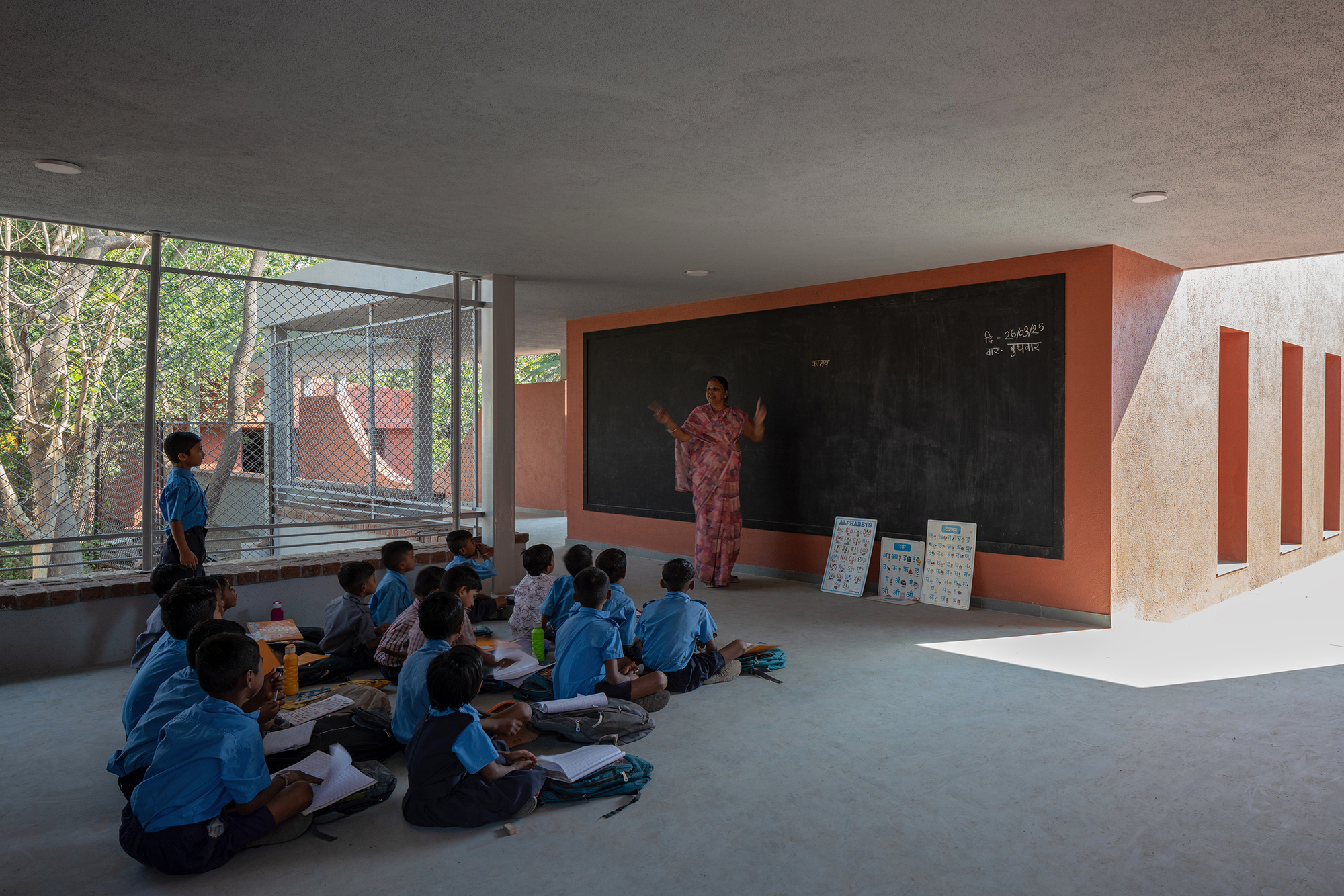Semi-open learning space with chalkboard wall and mesh-screened opening framing courtyard beyond