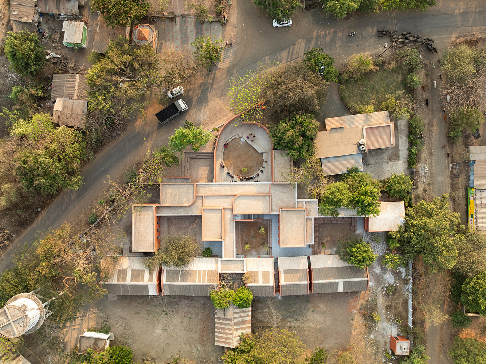 Aerial view of the building showing clustered flat roofs and circular amphitheater among trees and surrounding fields