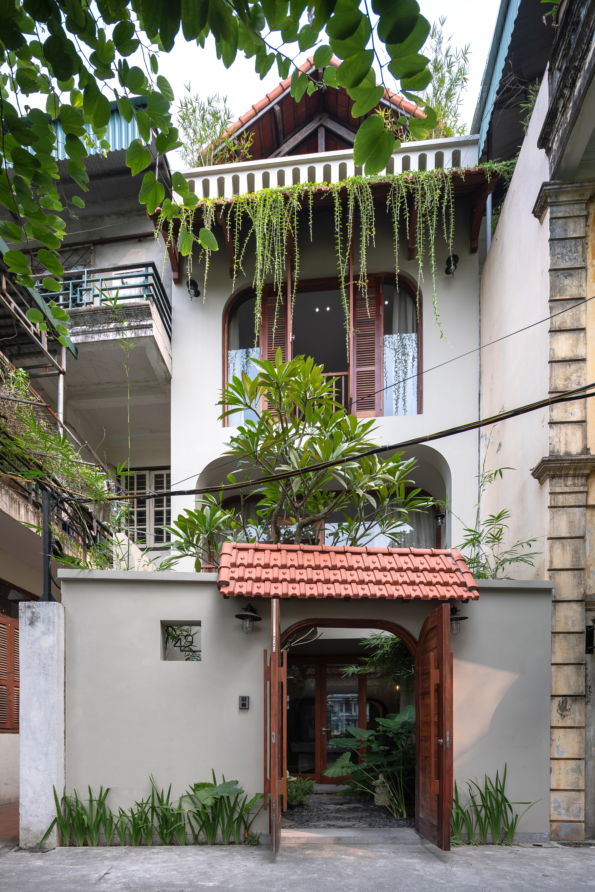 Street facade with timber-framed entry gate, terracotta tile roof and cascading plants from upper balcony
