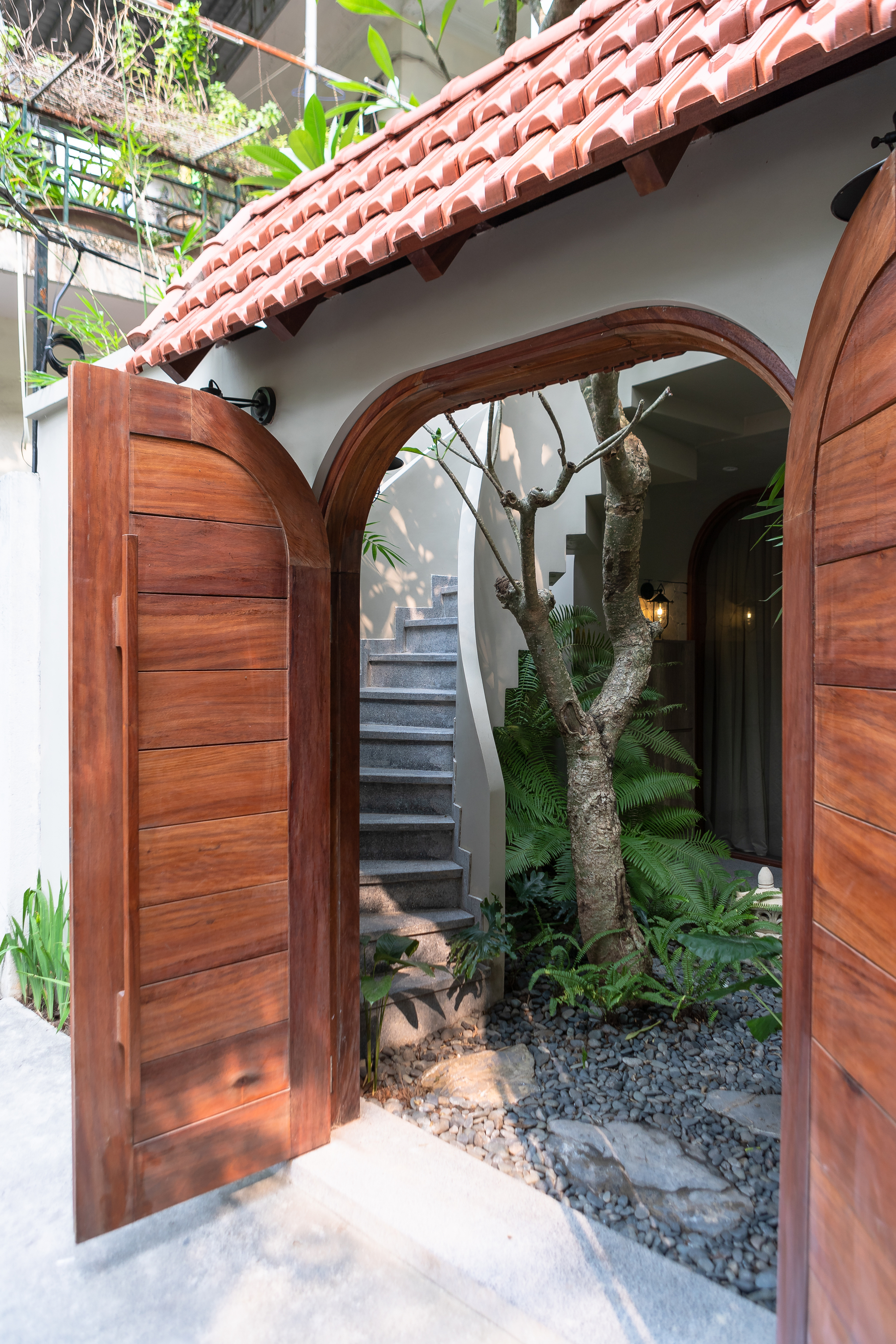 Arched timber doorway opening to a courtyard with terrazzo flooring, planted tree, and terracotta tile roof