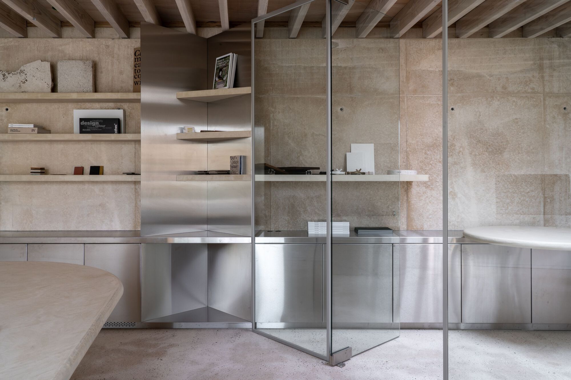 Interior shelving with plywood surfaces and stainless steel base cabinets reflected in glass partition
