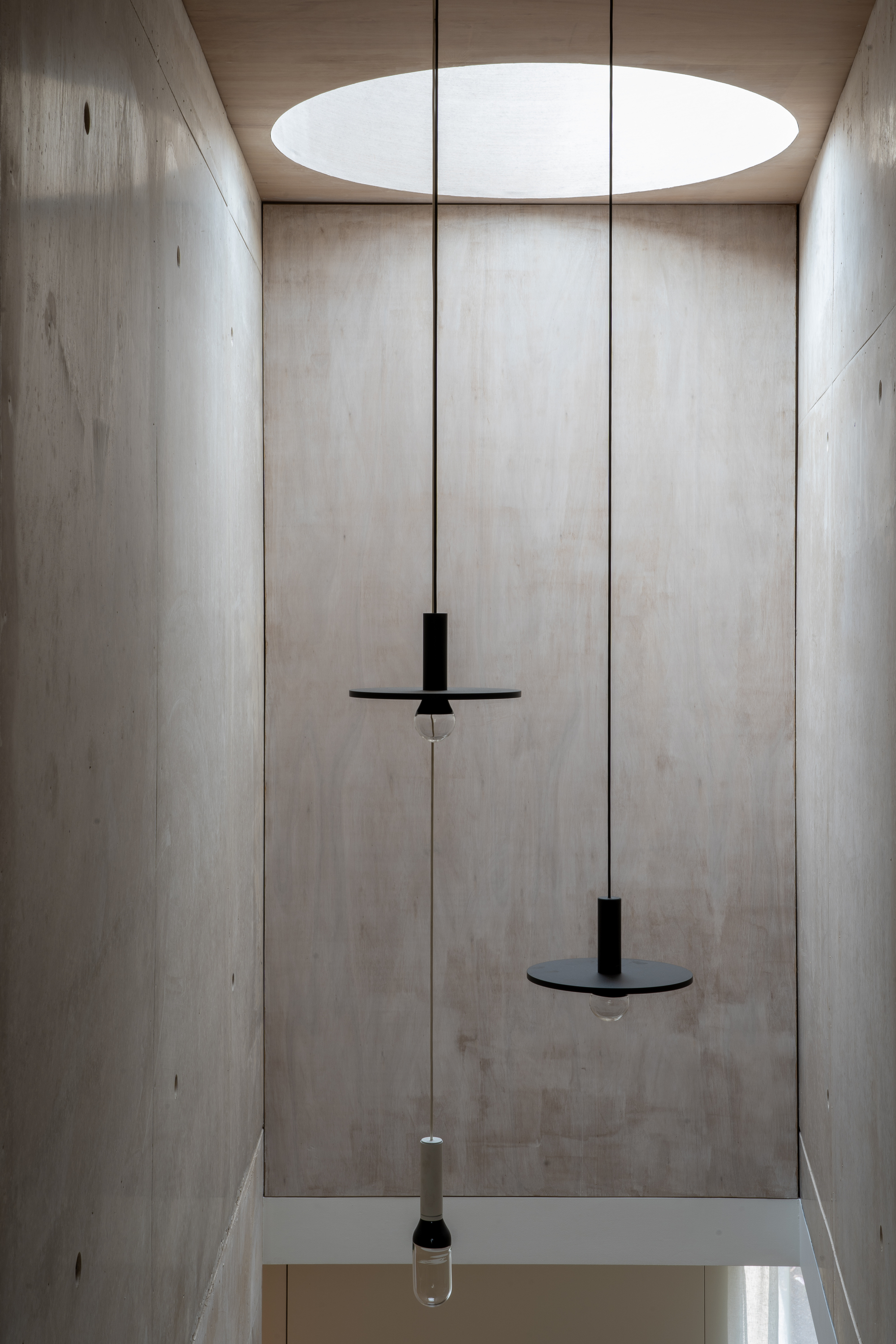Double-height concrete stairwell with circular skylight and suspended black pendant fixtures