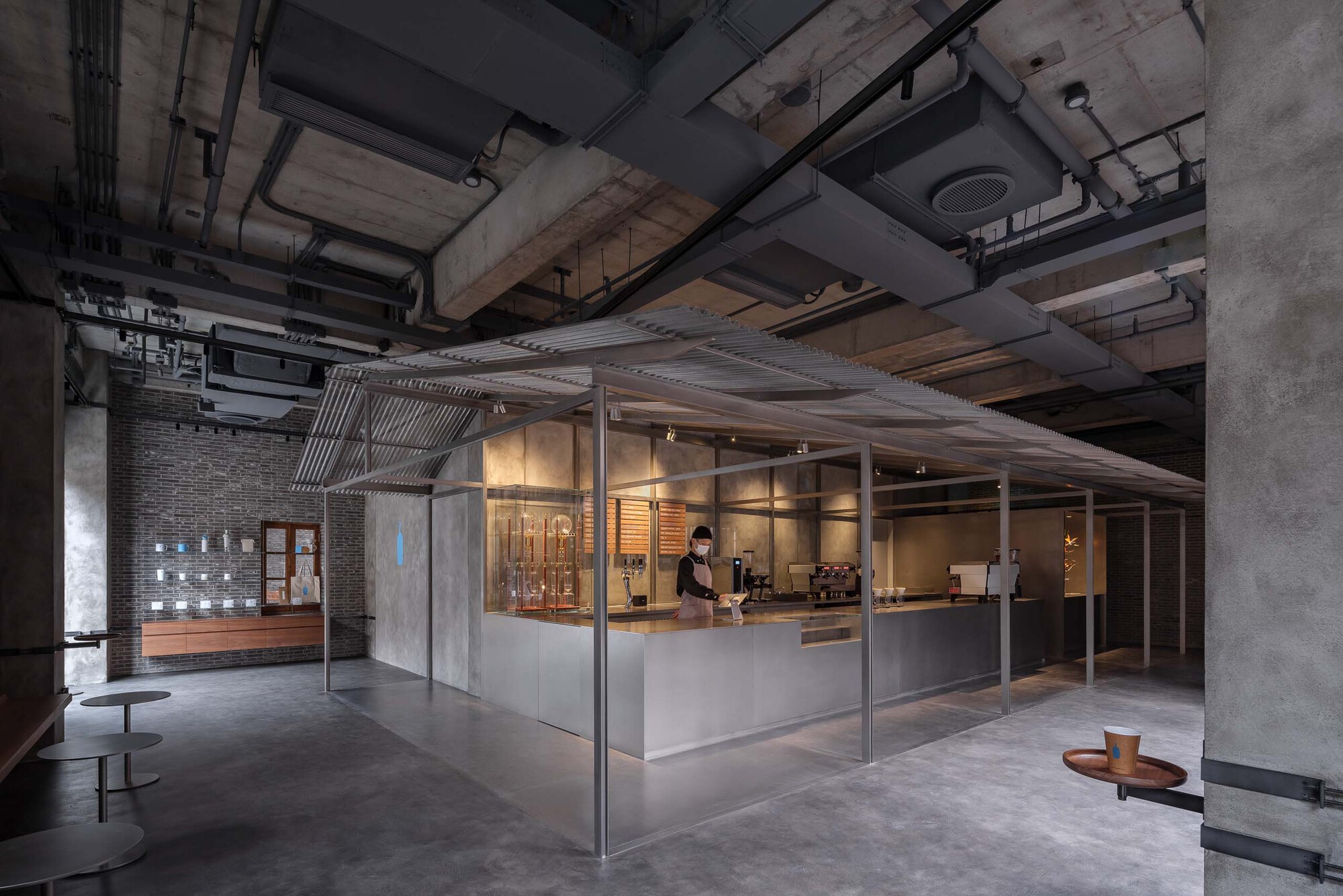 Angular view of the glazed service pavilion with metal frame and corrugated ceiling beneath exposed concrete beams