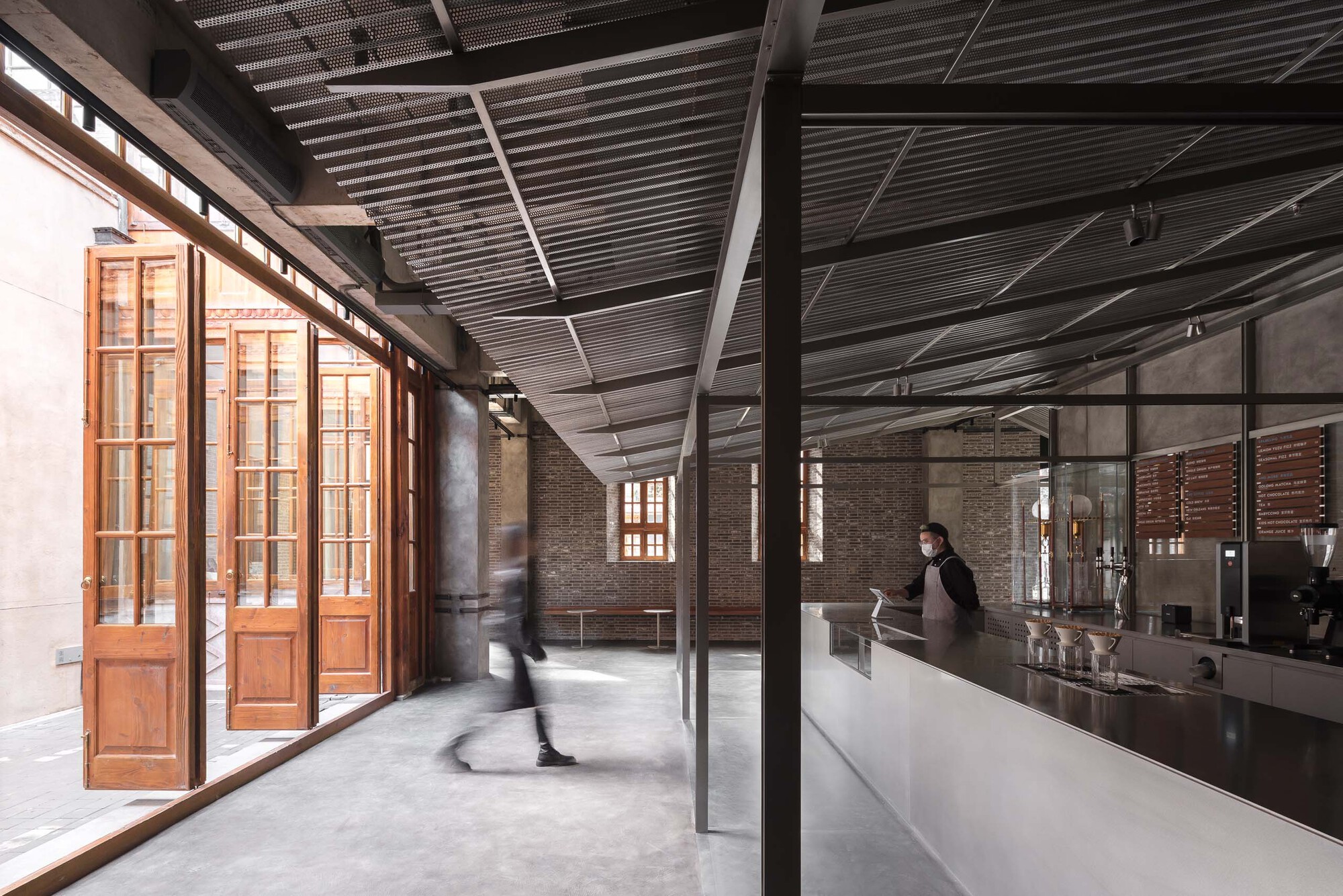 Interior corridor with polished concrete floor, timber doors, and corrugated metal ceiling as a patron walks past