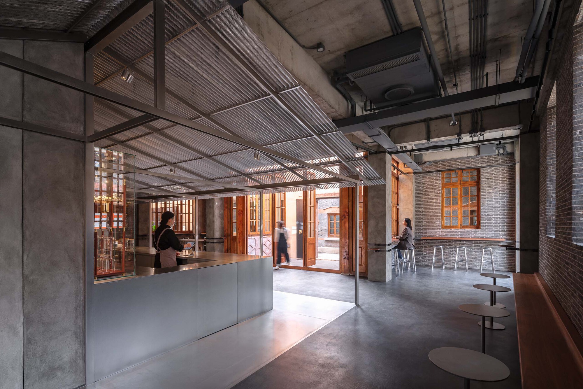 Cafe counter and seating area with exposed structural beams and people moving through the space