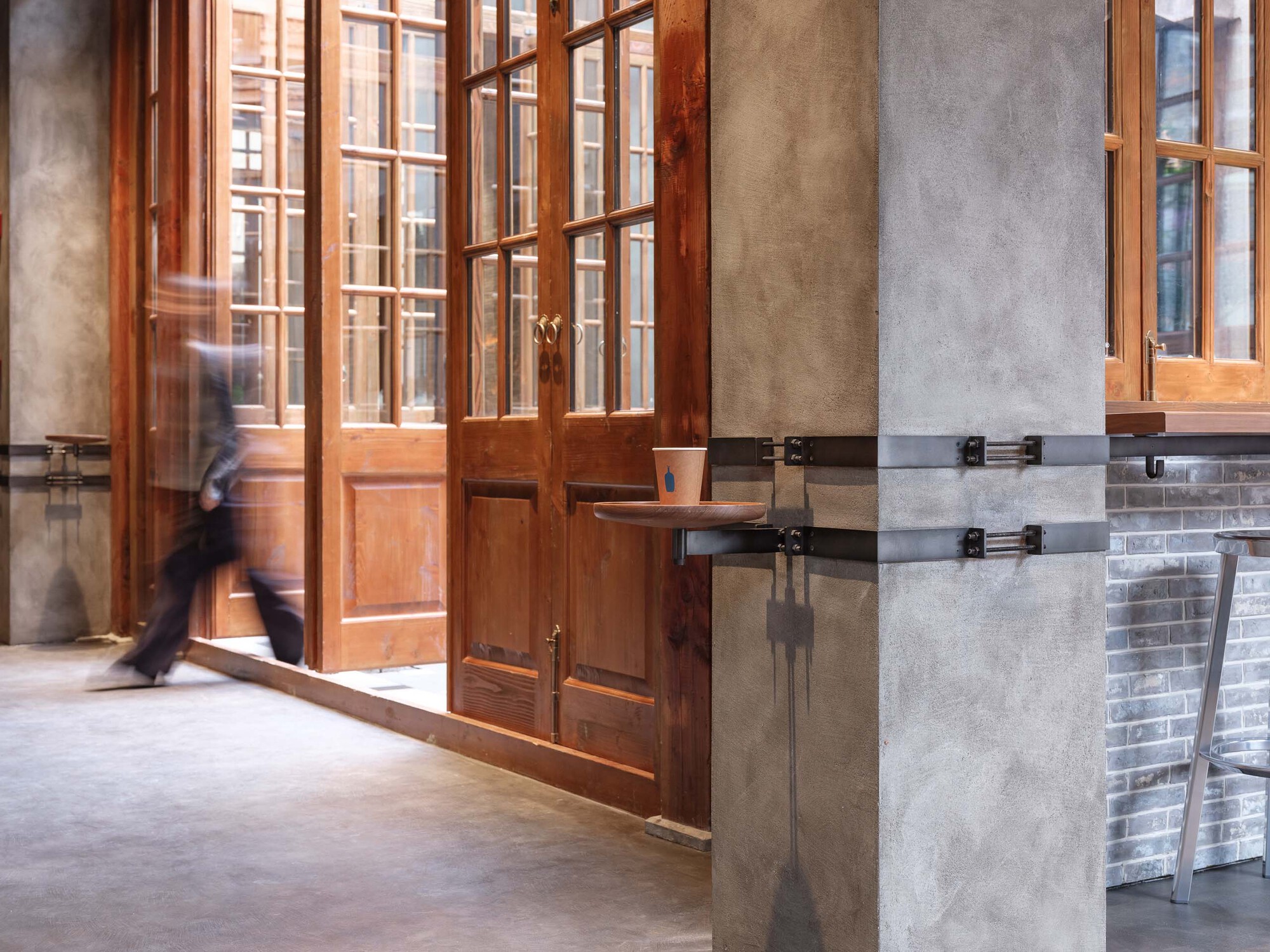 Detail of timber-framed doors with concrete column wrapped in steel straps as person passes through
