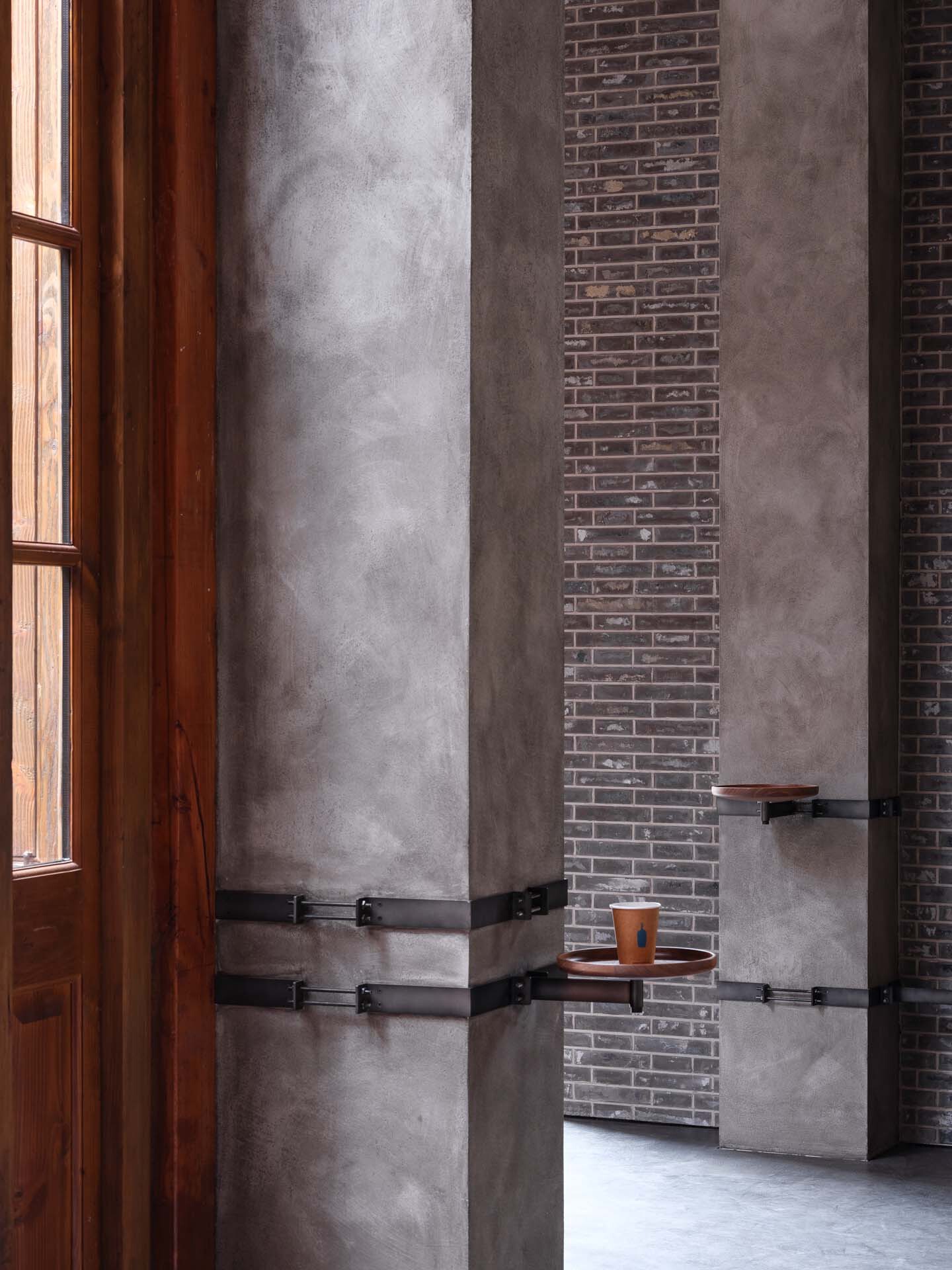 Concrete column with black metal banding beside a timber window frame and brick wall