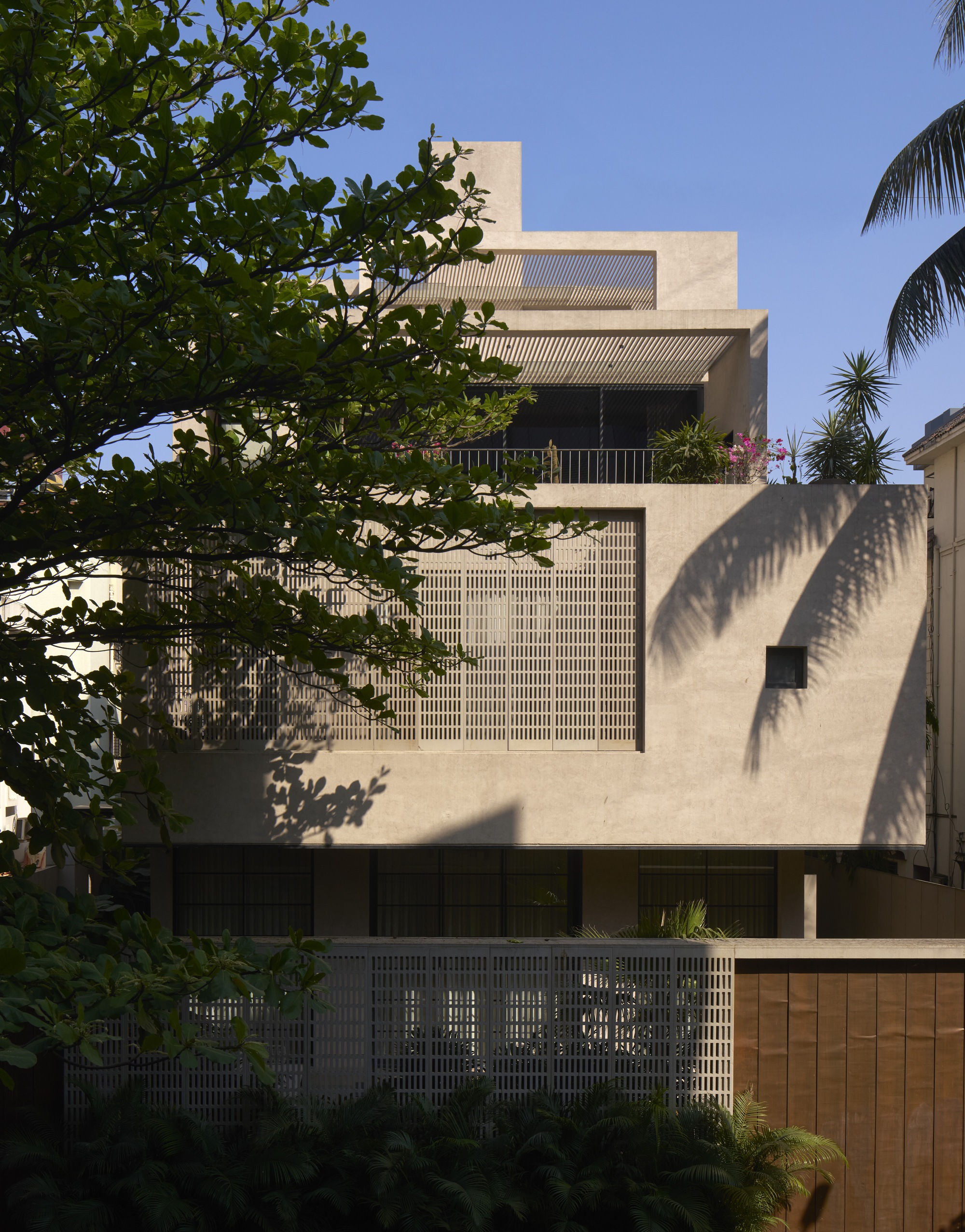 Street facade with stacked volumes and gridded brickwork screens framed by palms and tropical trees