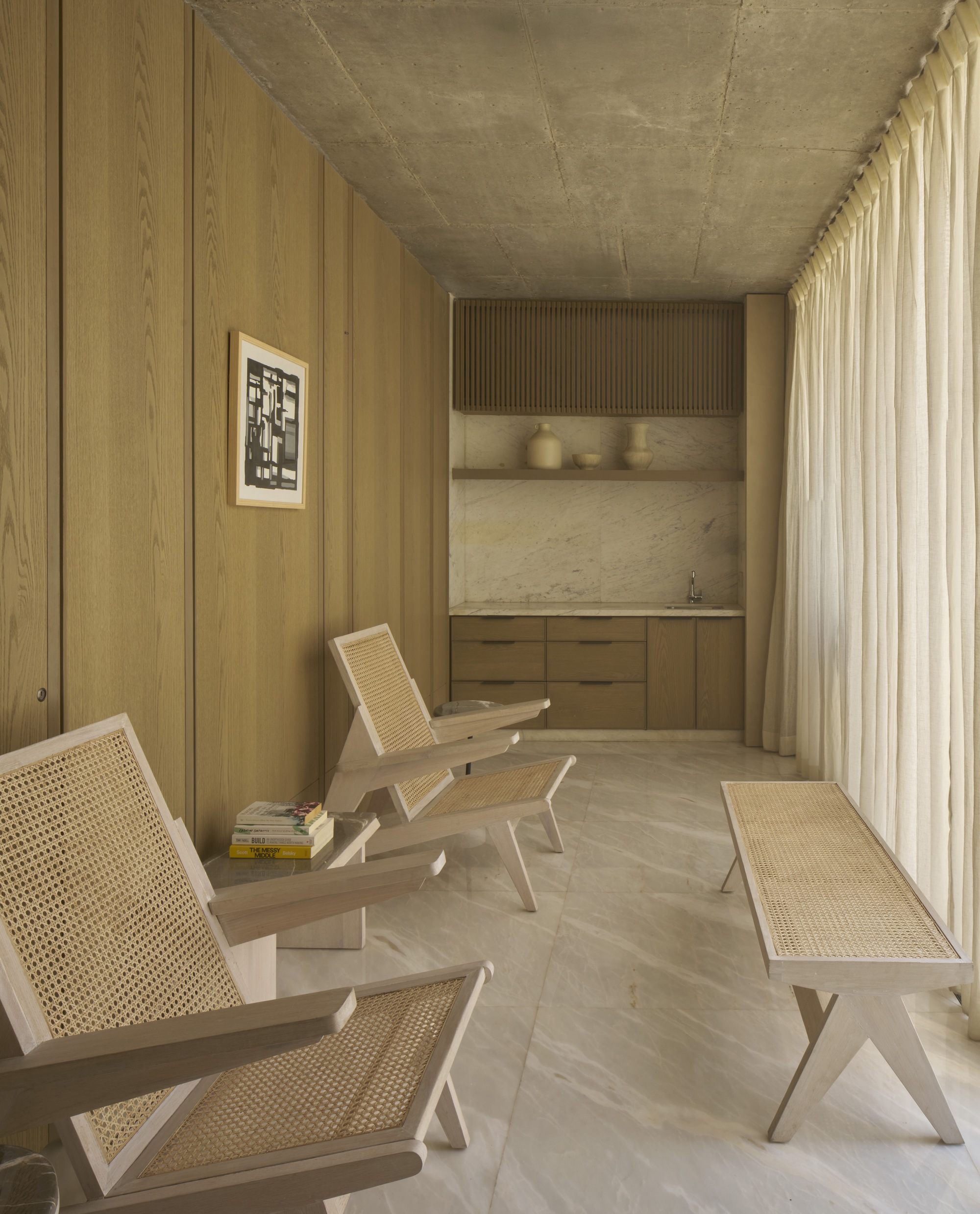 Timber-paneled room with cane-backed seating and a recessed kitchenette behind sheer curtains