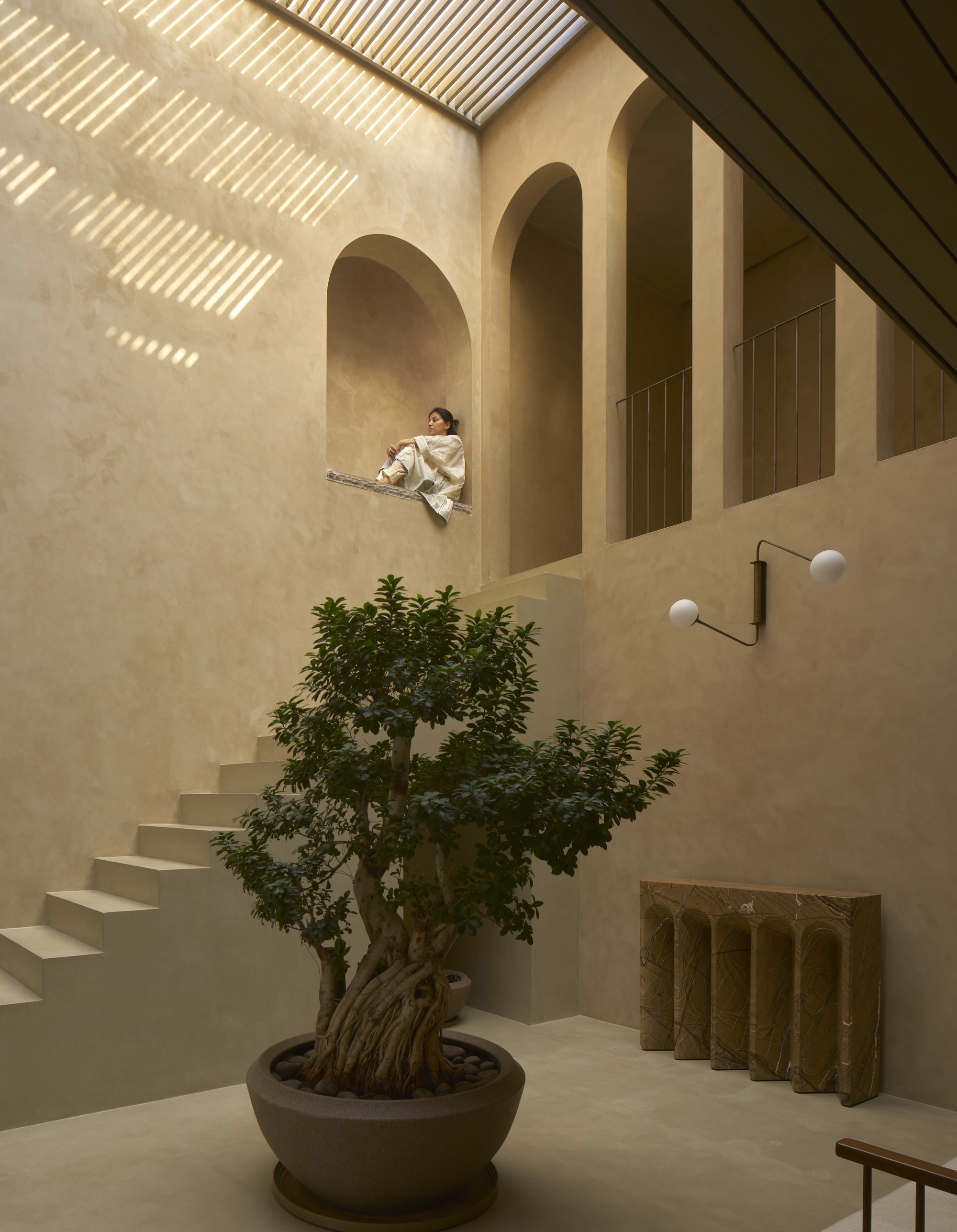 Multi-level courtyard with arched openings, floating stairs, and a person seated in an alcove above