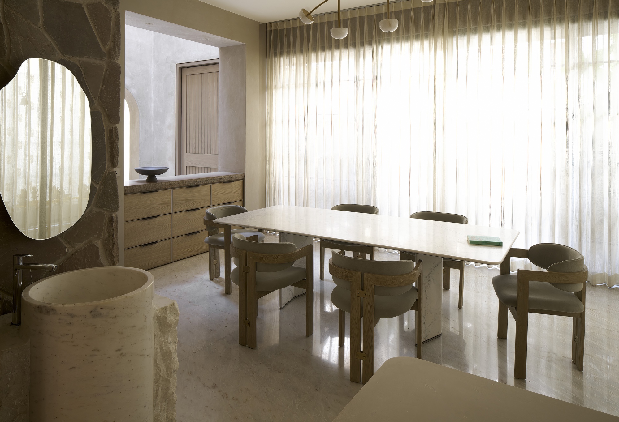 Dining area with timber table and chairs beside a dark marble portal and sheer curtain wall