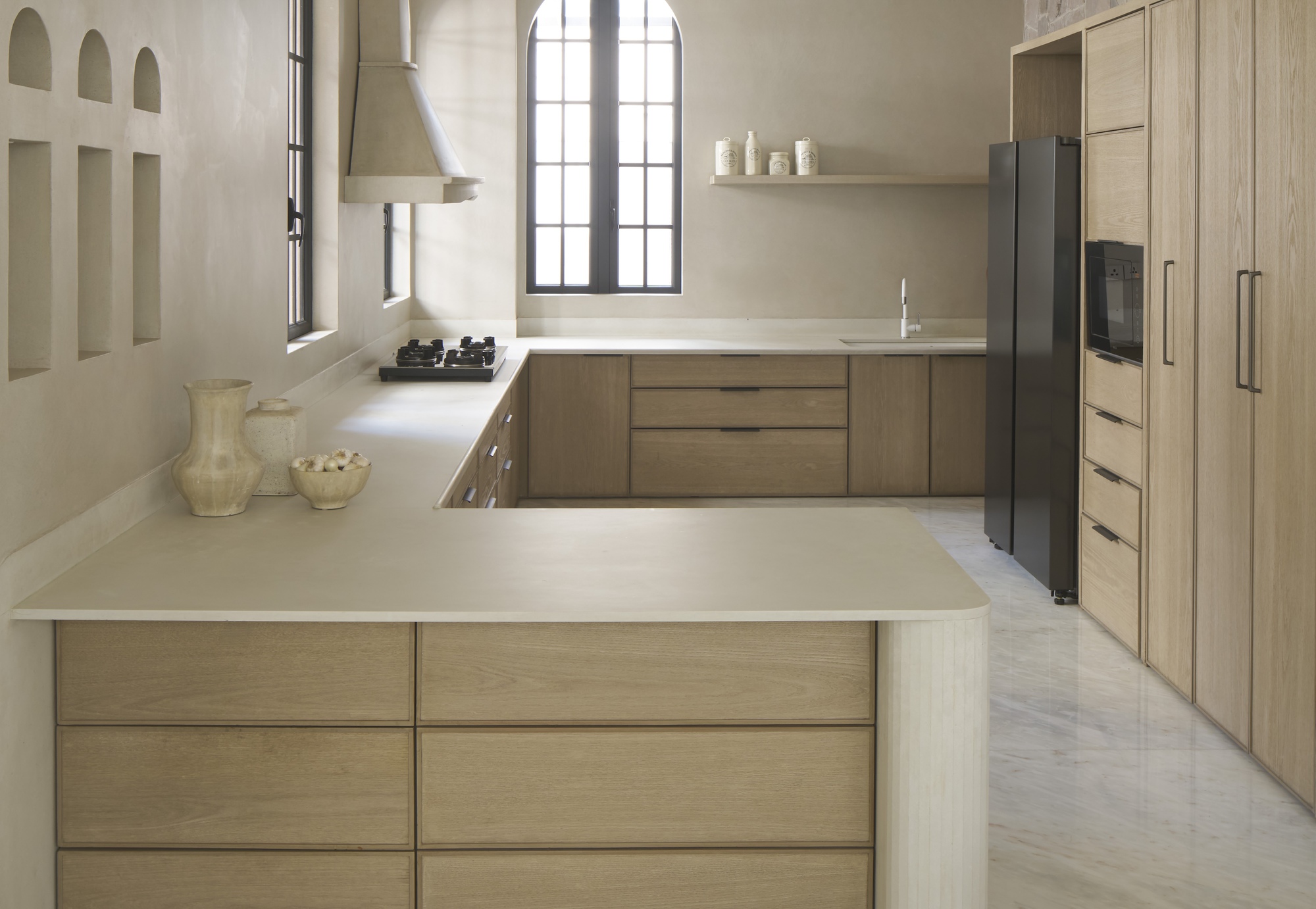 Kitchen with oak cabinetry and island beneath arched window with steel frame muntins