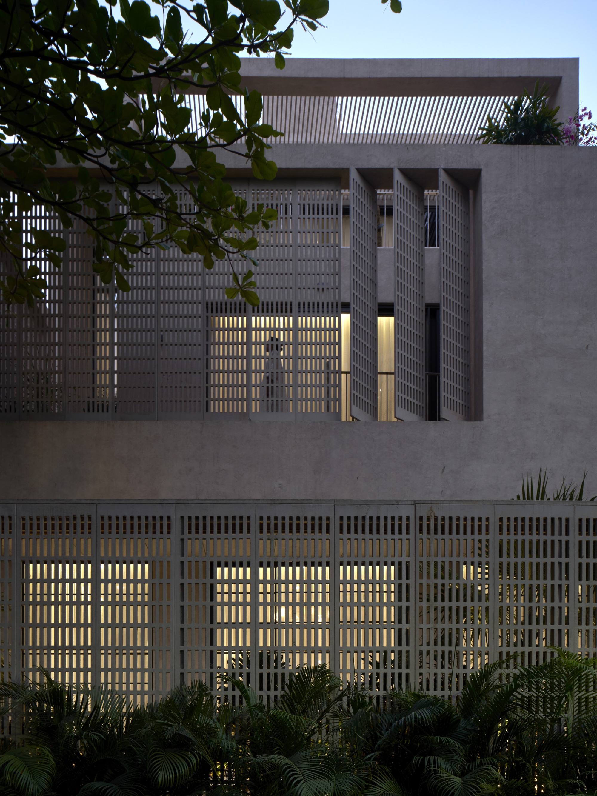 Street view of stacked volumes with brise-soleil screens and planted foreground at twilight