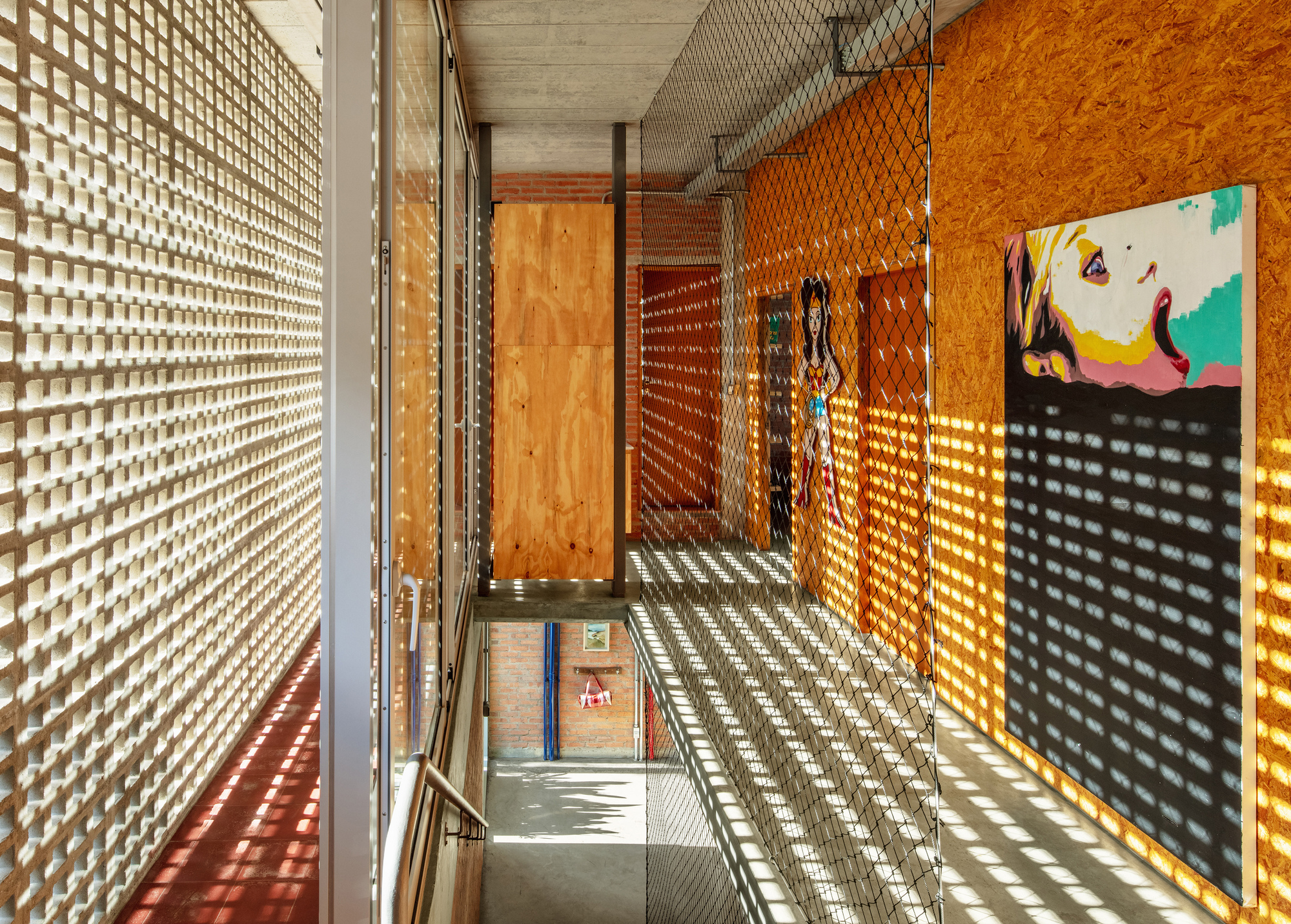 Stairwell with perforated block walls casting latticed shadow patterns across plywood panels and concrete floor