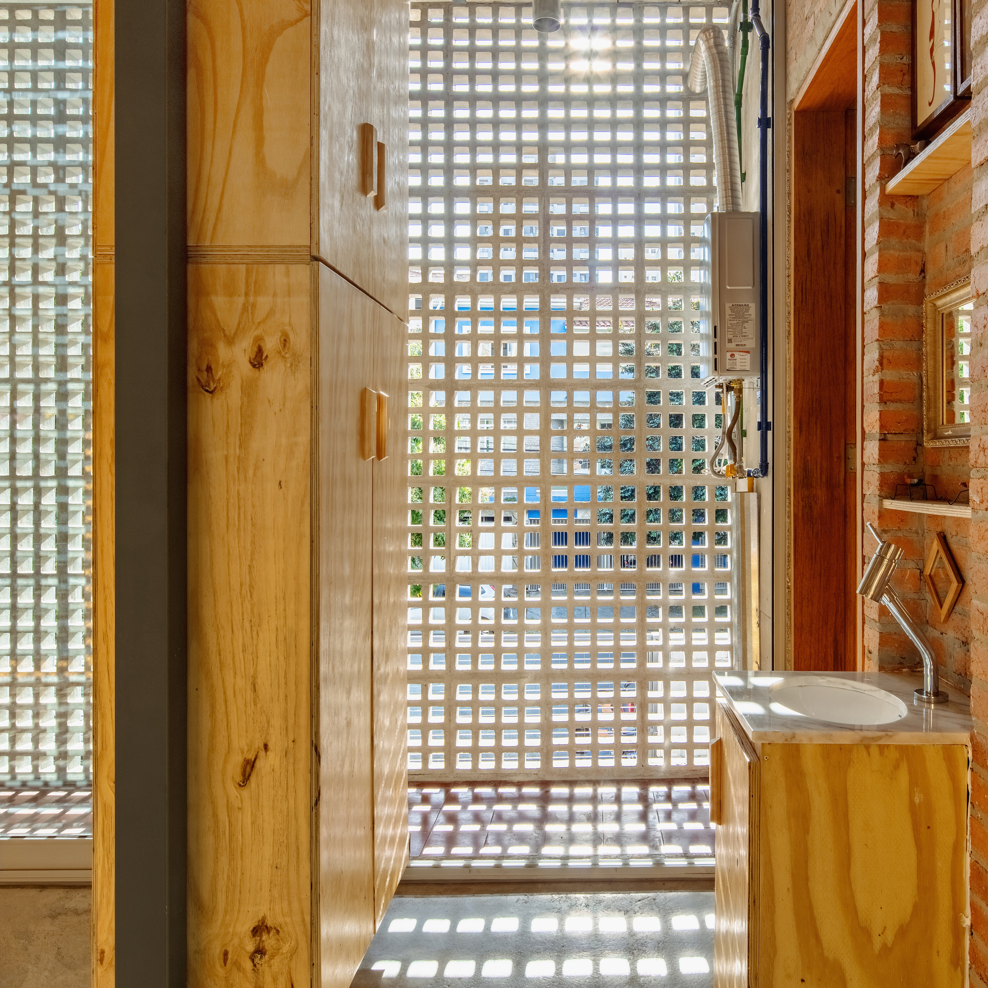 Bathroom corridor with glass block wall filtering daylight onto plywood cabinetry and concrete floor