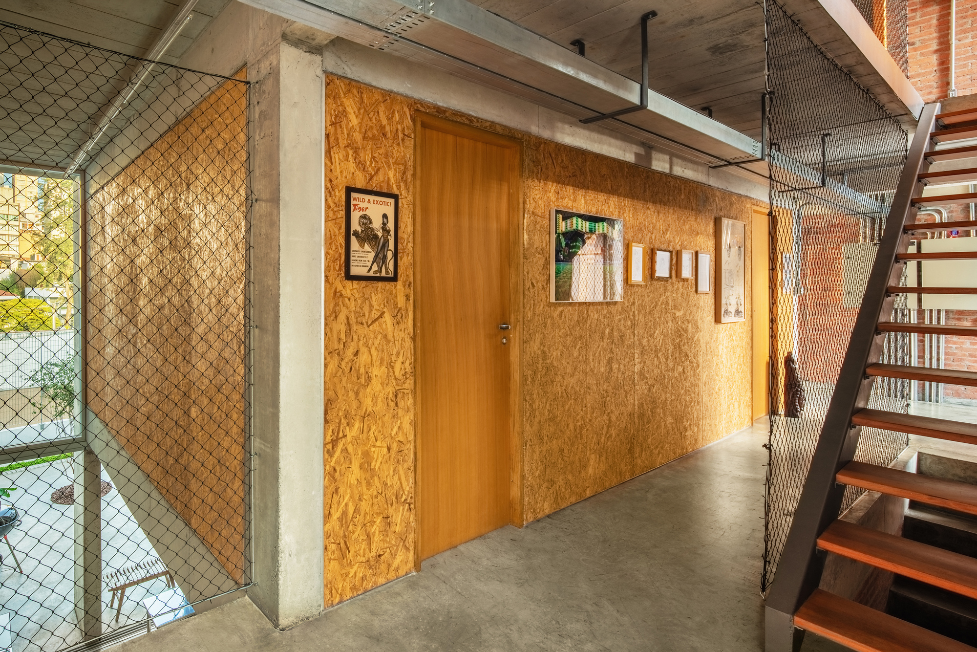 Upper hallway with oriented strand board wall and chain link mesh stair railing