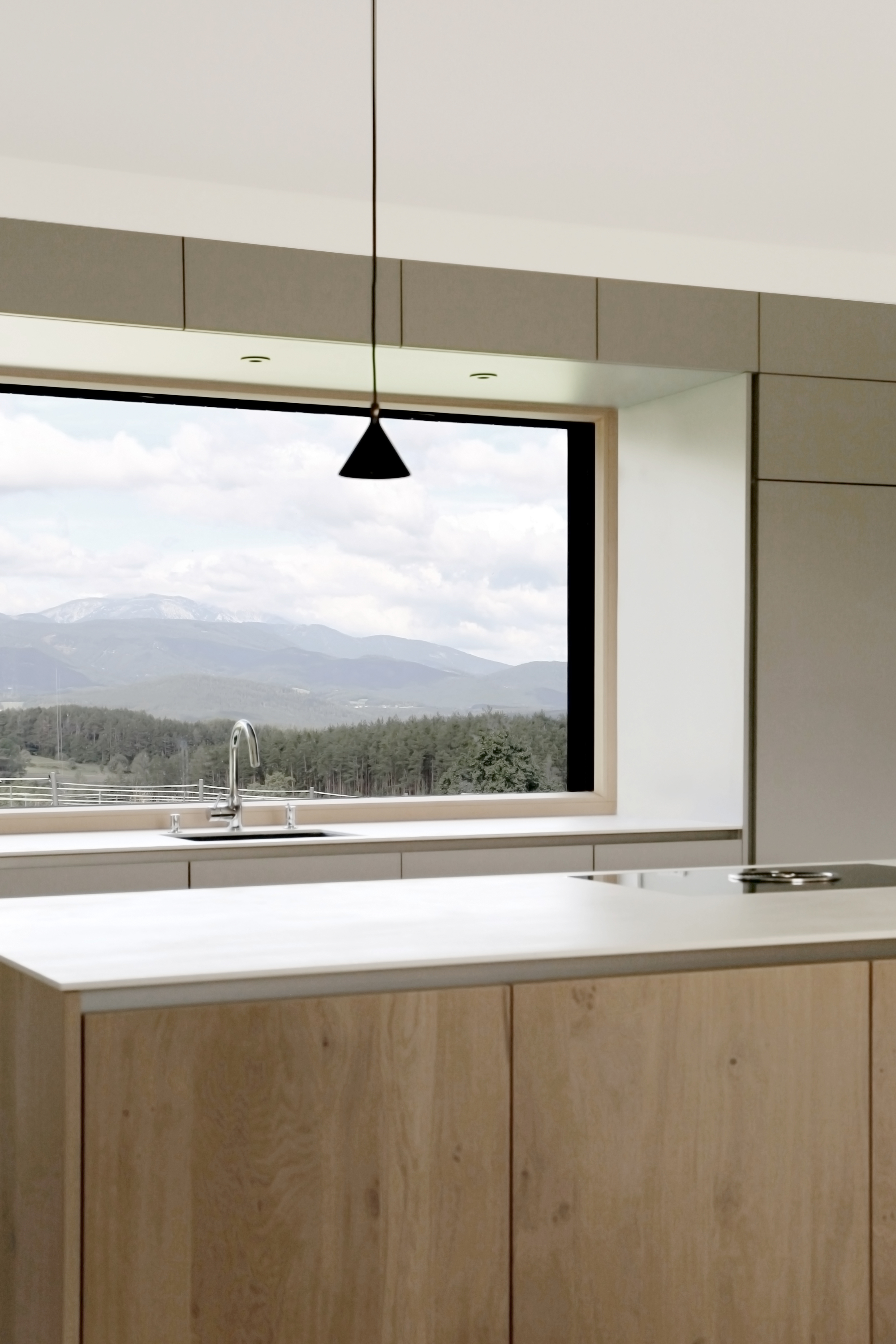 Kitchen island with light timber cabinetry and horizontal window framing a view of forested mountains