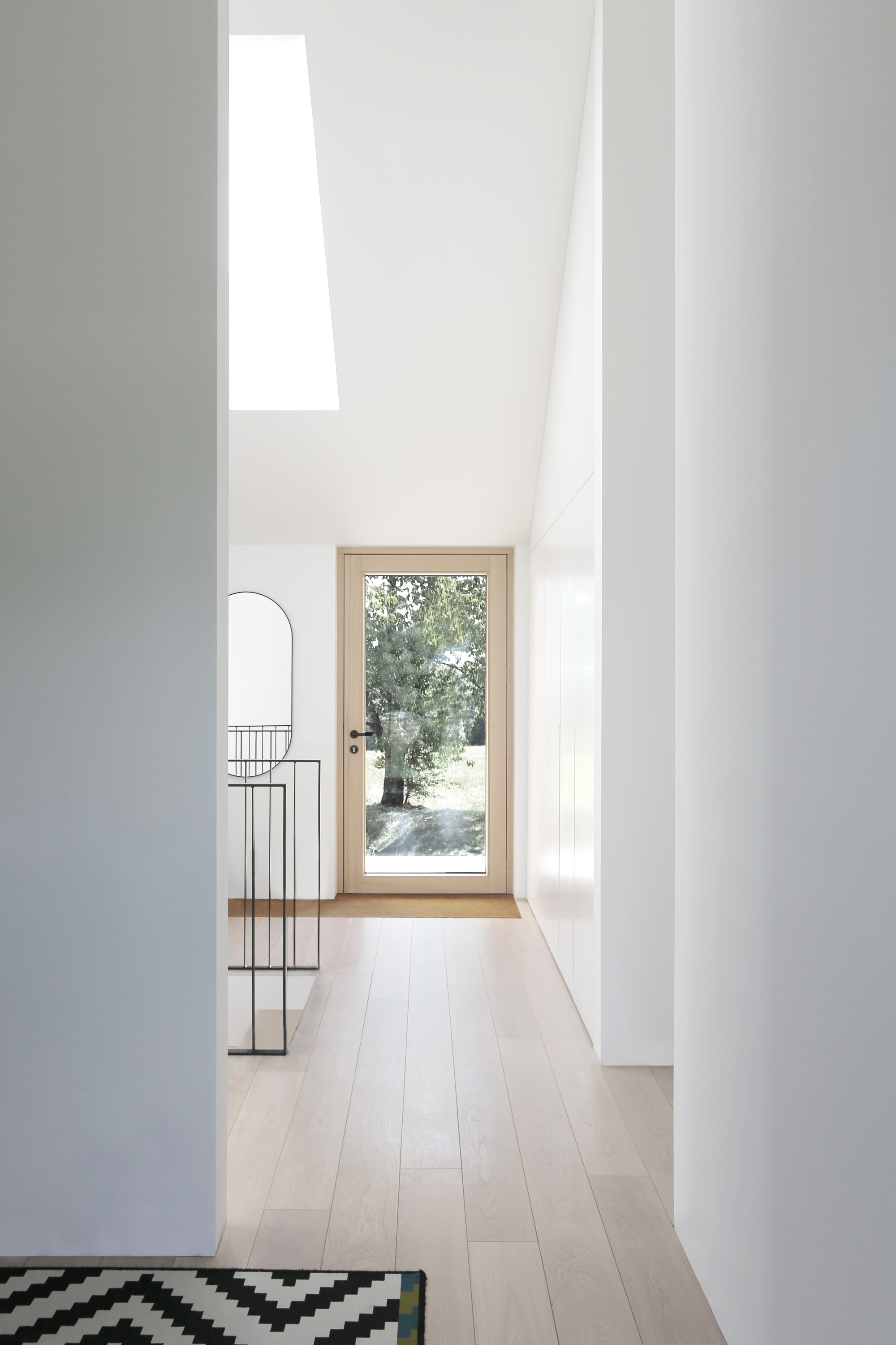 White corridor with light wood flooring leading to a glass door framed with pale timber