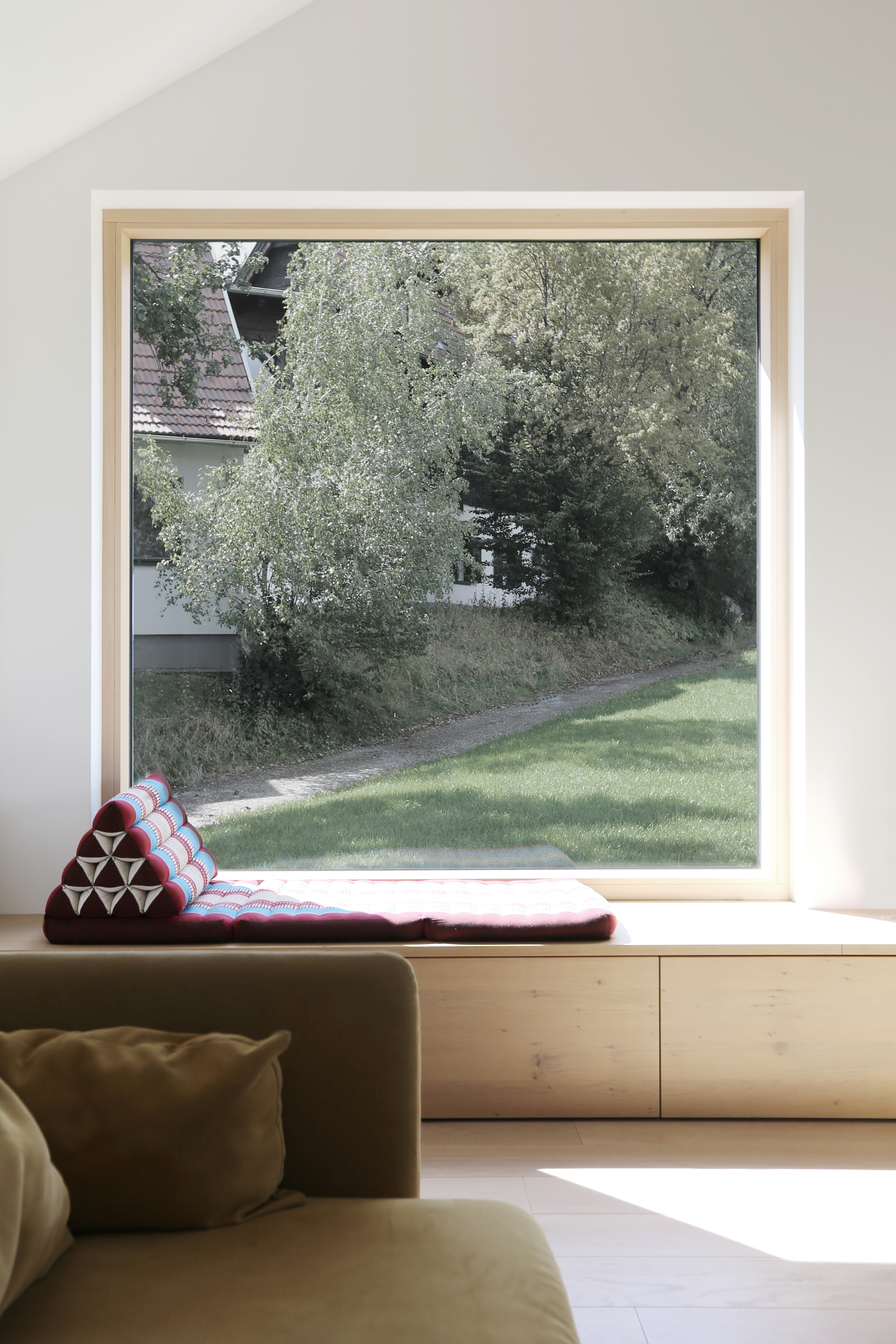 Built-in window seat with cushion overlooking lawn and trees through a large square timber window