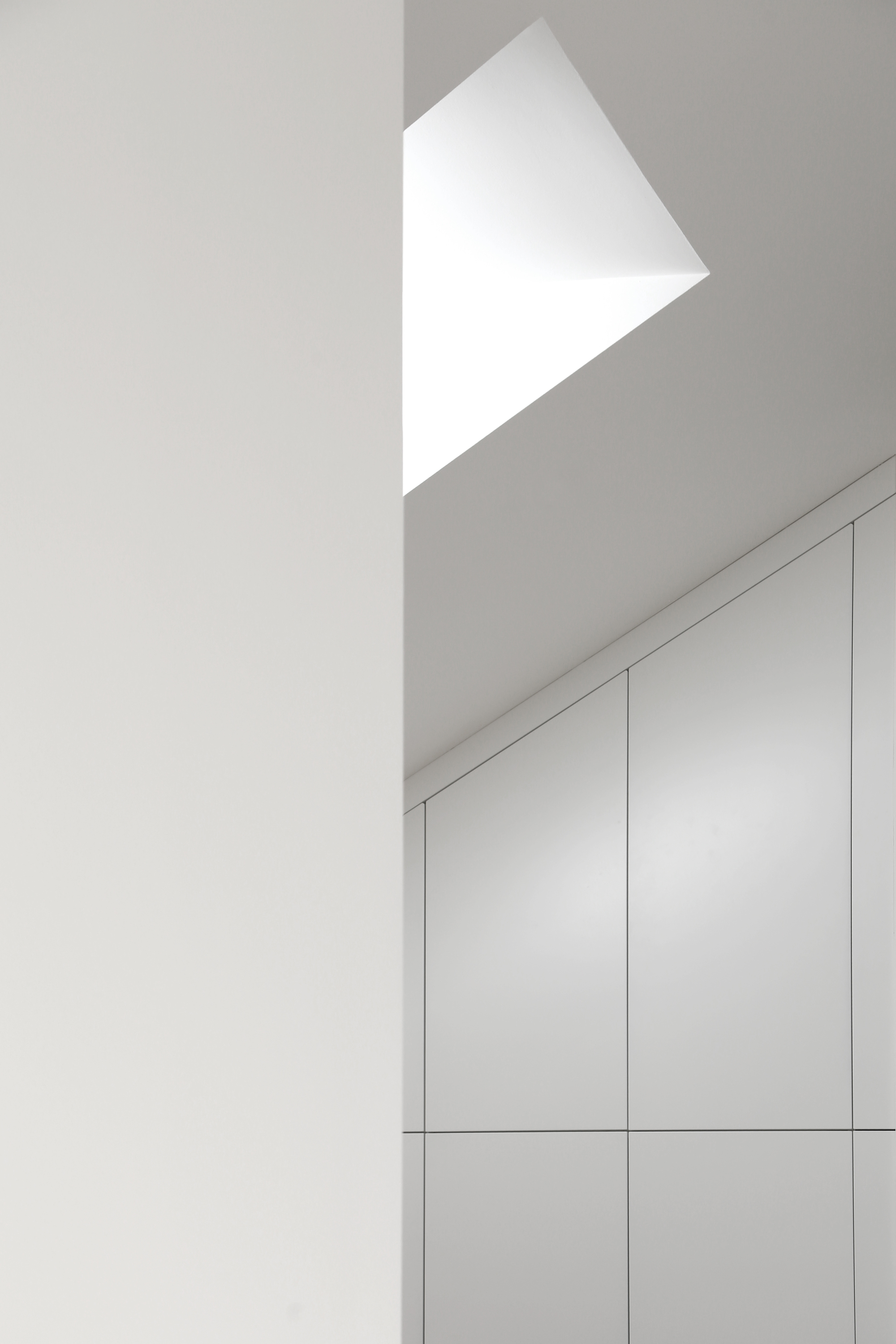 Angular skylight above white built-in cabinetry casting geometric shadows on the ceiling