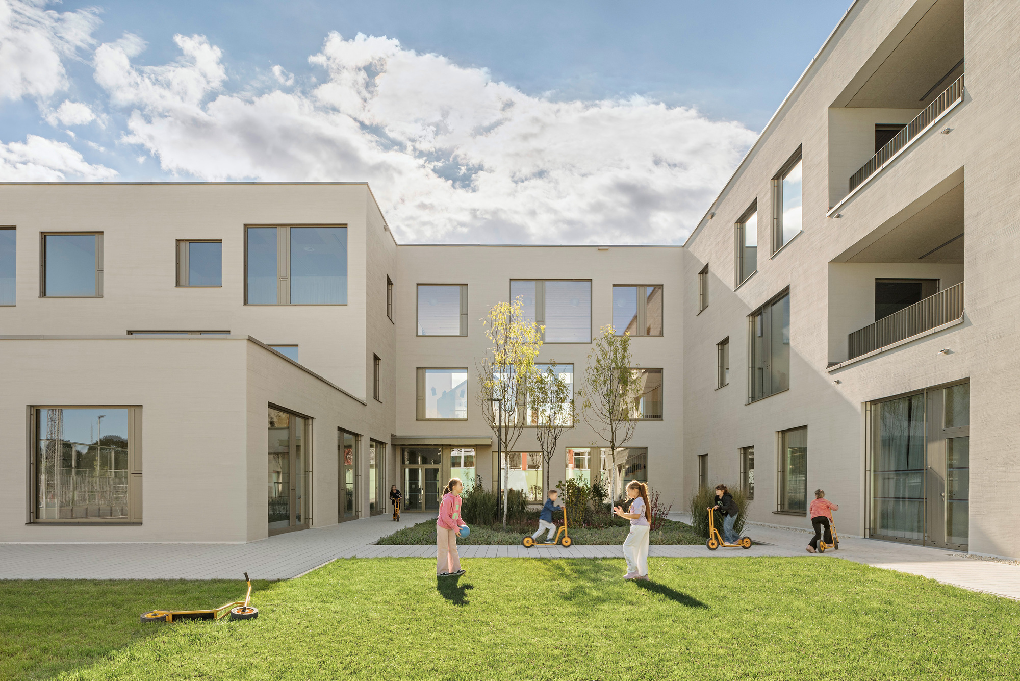 Courtyard with grass lawn and young trees surrounded by rendered facades under a bright sky