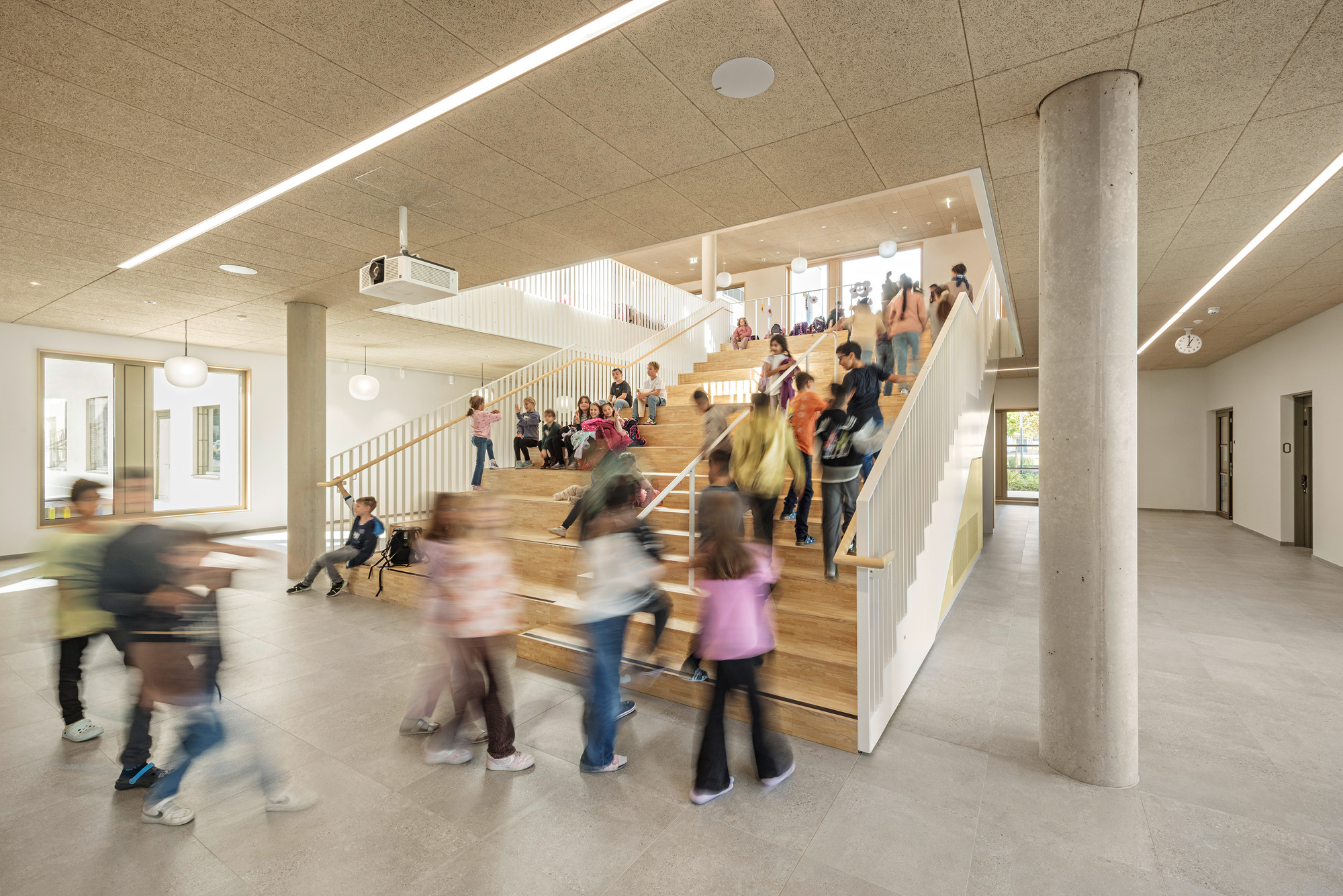 Wide timber staircase with children seated and moving through the double-height circulation space
