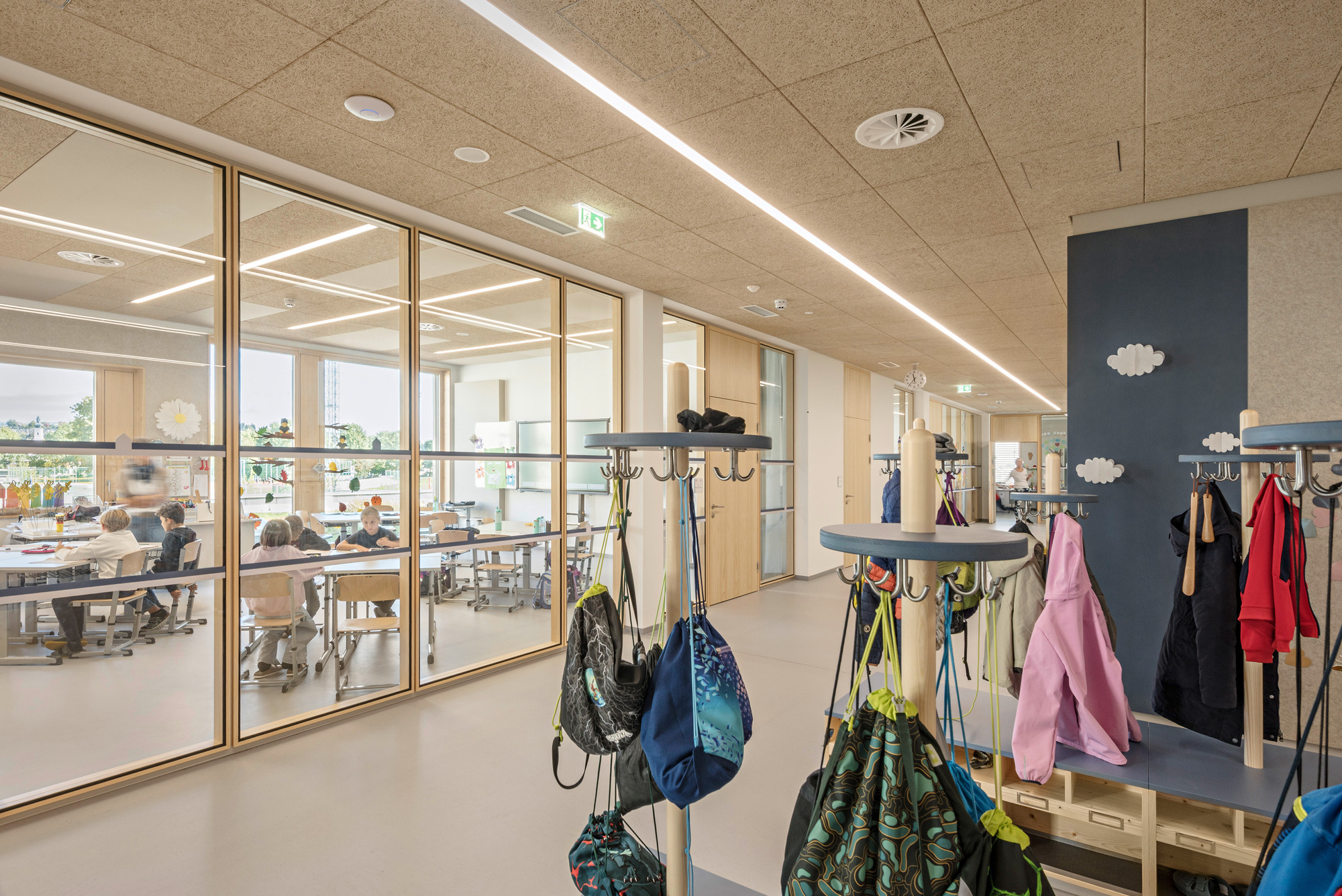 Interior hallway with coat hooks and glazed partition looking into adjacent classroom spaces