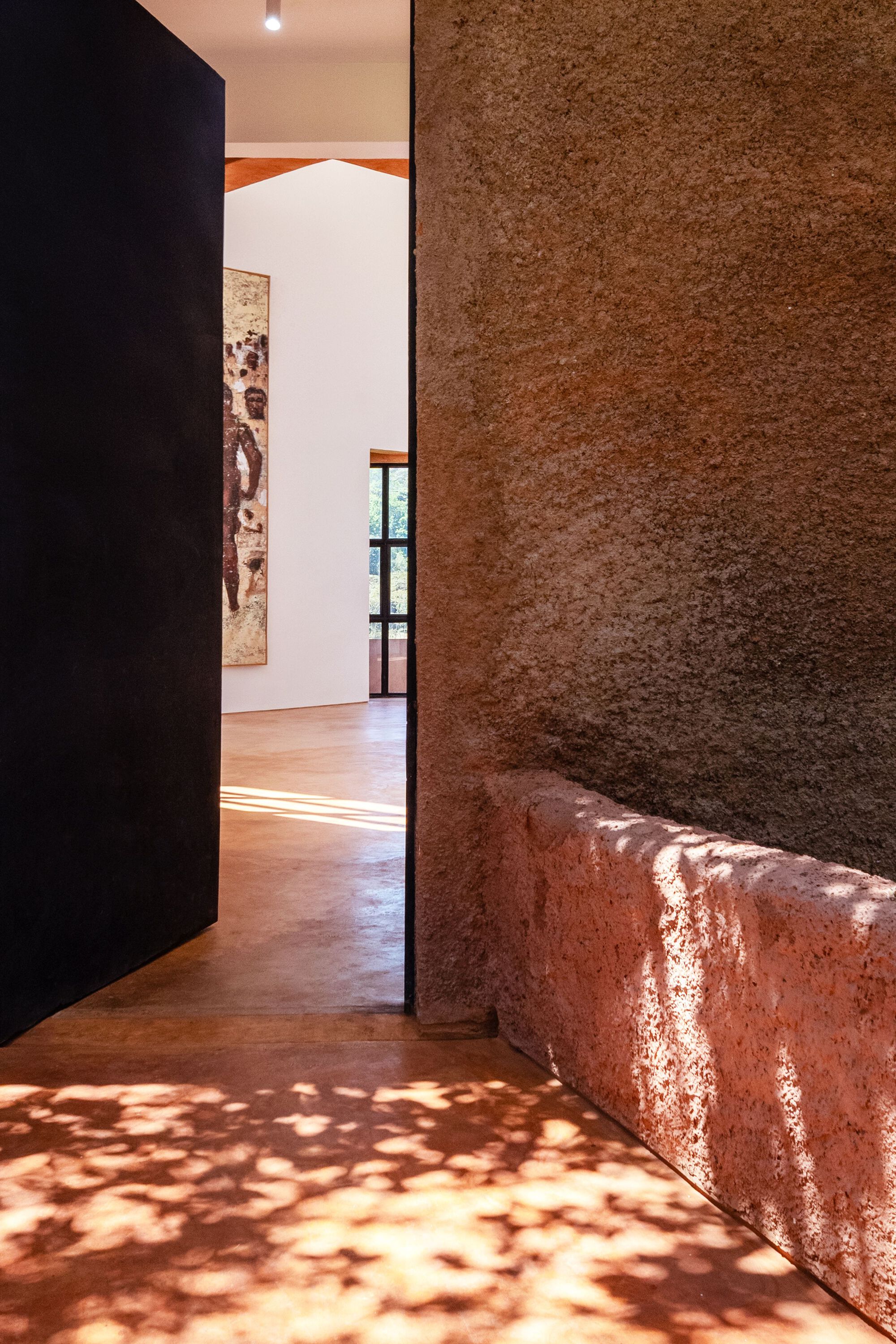 Entry threshold with rammed earth wall and bench catching dappled afternoon light on polished floor