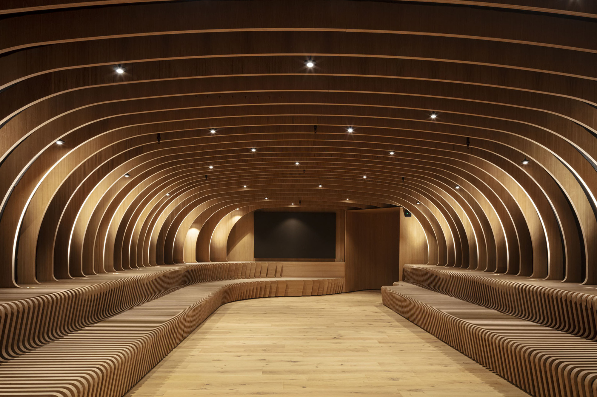 Arched timber ribs forming continuous walls and ceiling with integrated bench seating and recessed spotlights