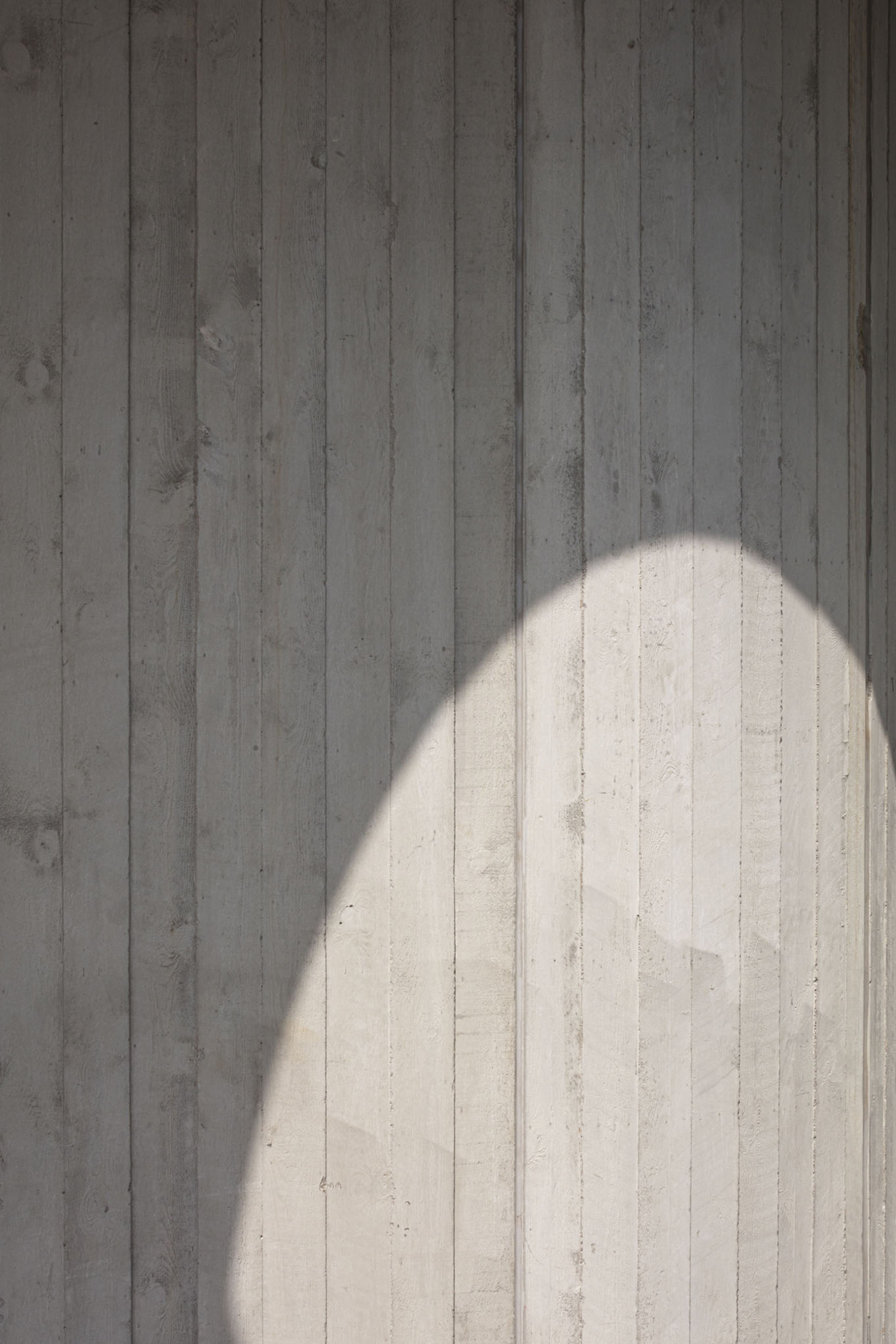 Board-formed concrete wall with an arched shadow cast by overhead structure