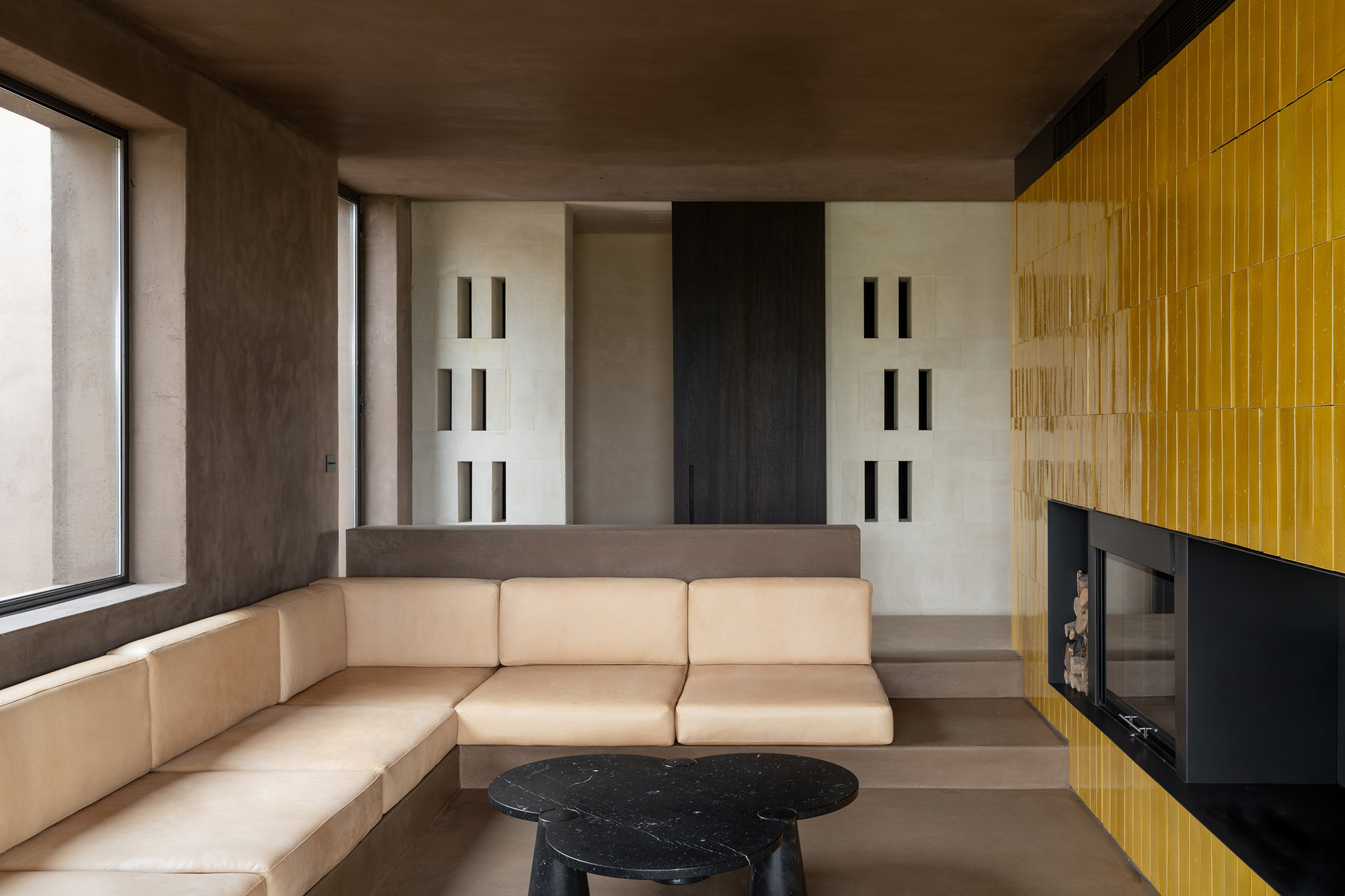 Living room with built-in sectional sofa, yellow fluted wall, and vertical window slits