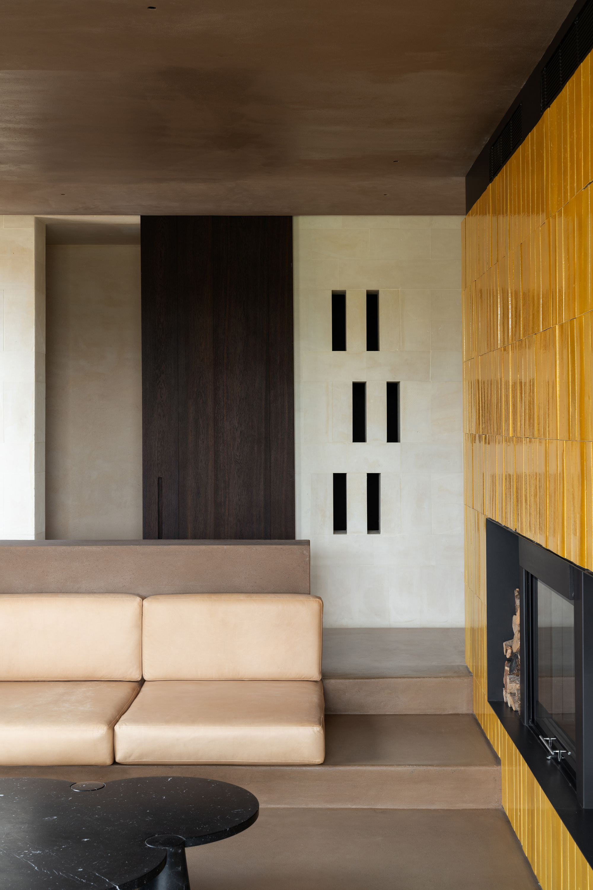 Interior view showing timber fireplace surround and built-in seating beside vertical slot openings in wall