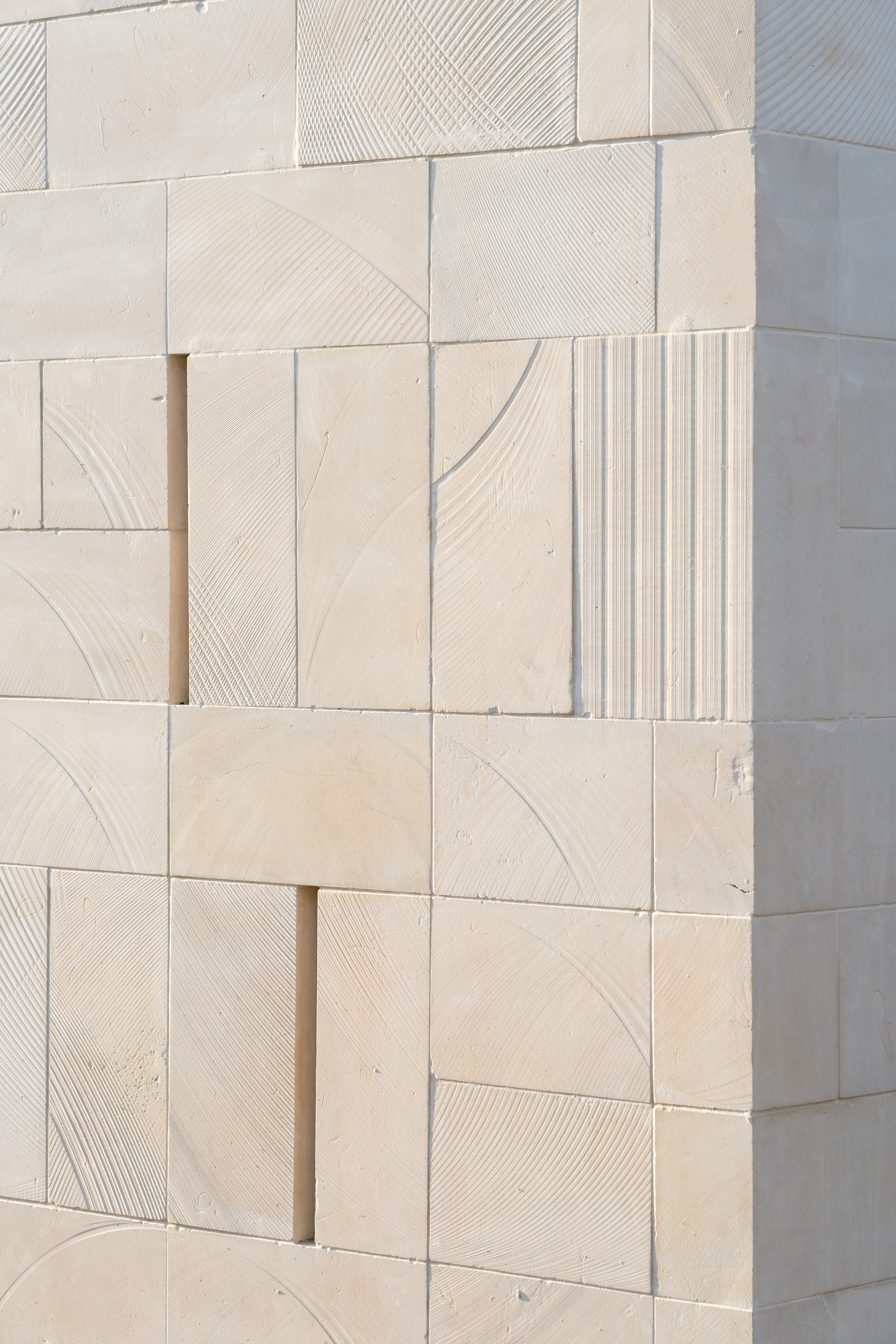 Close-up of pale limestone wall cladding with varied surface textures including smooth, striated, and fluted finishes